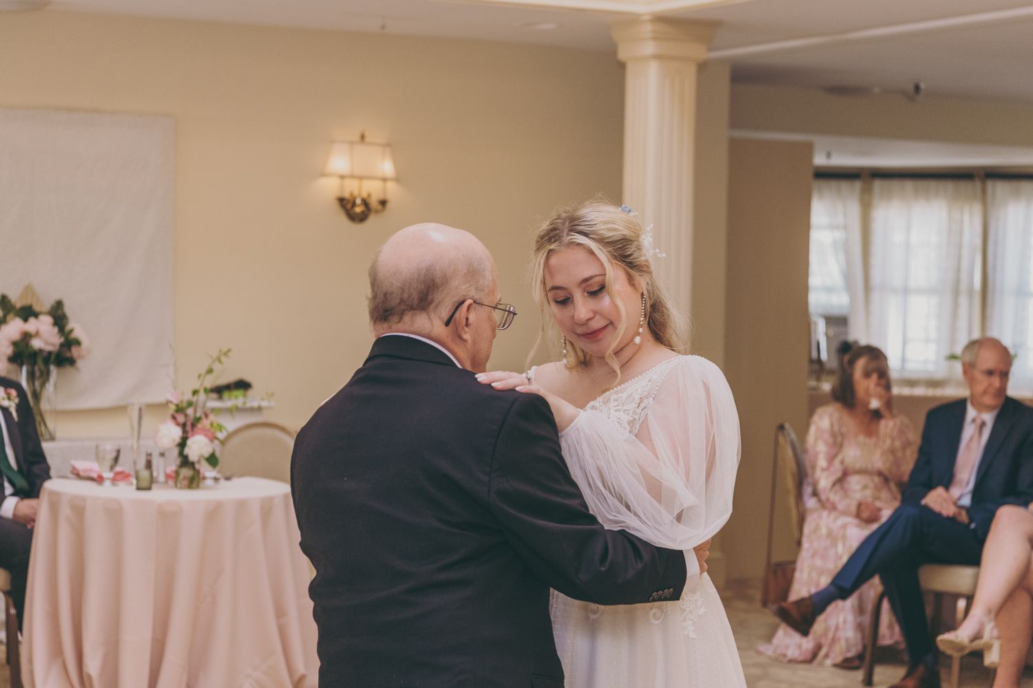 A bride shares an emotional father-daughter dance at her wedding reception indoors.