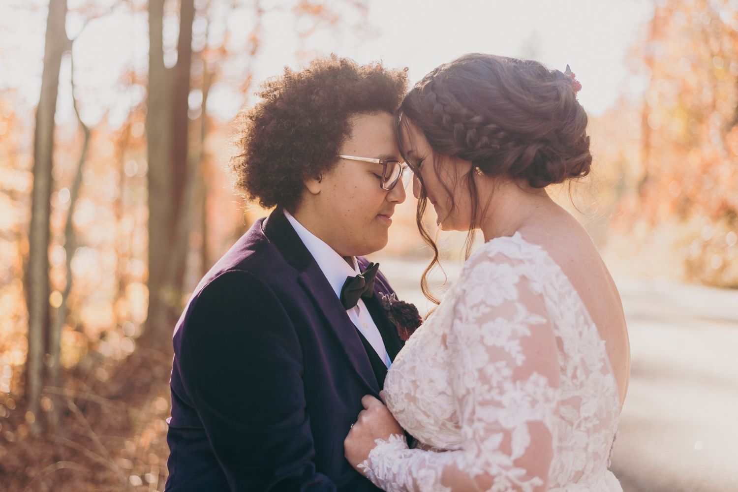 Couple in wedding attire sharing an intimate moment outdoors amid autumn foliage.