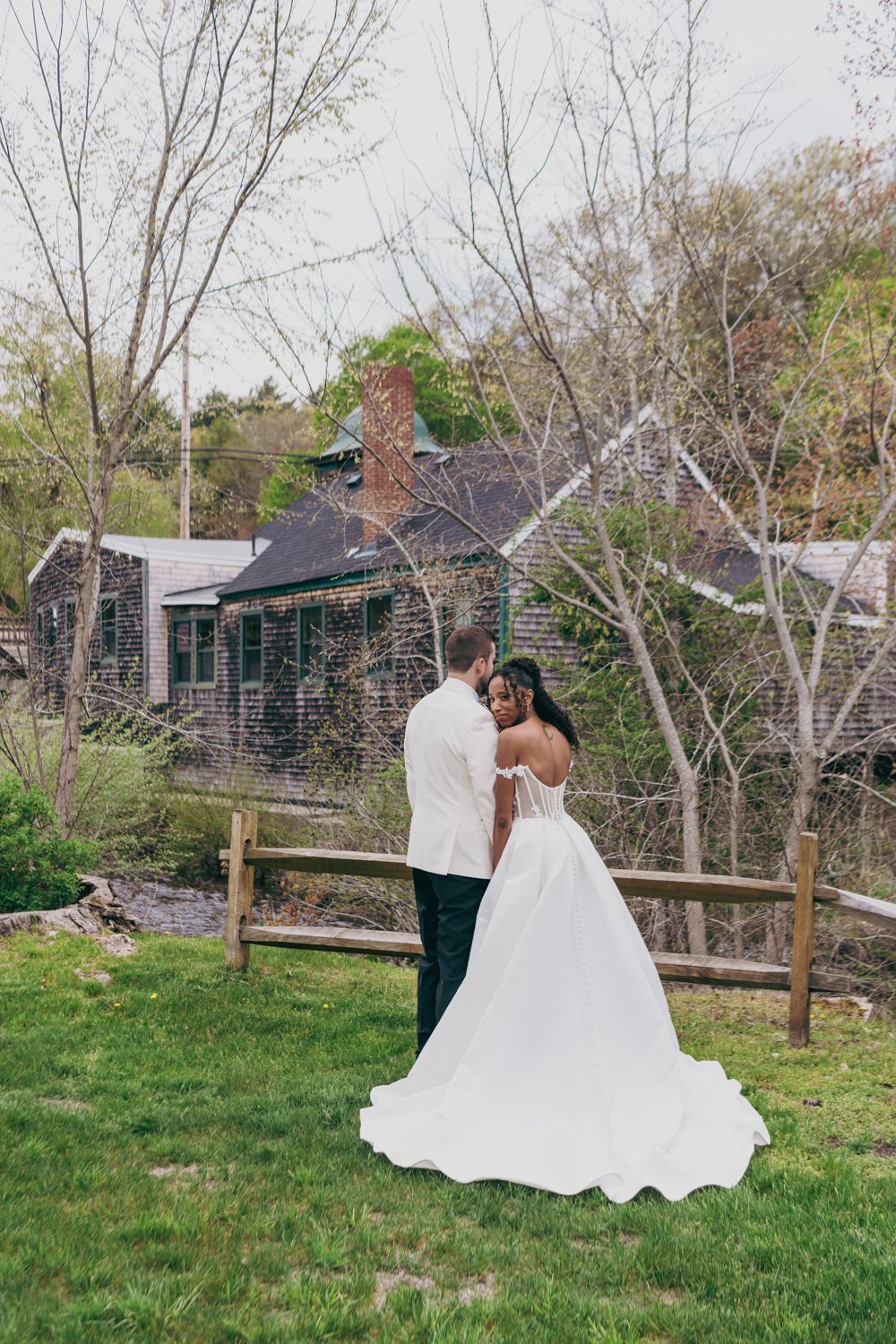 Bride and groom share romantic moment in lush garden outside rustic stone building on wedding day.