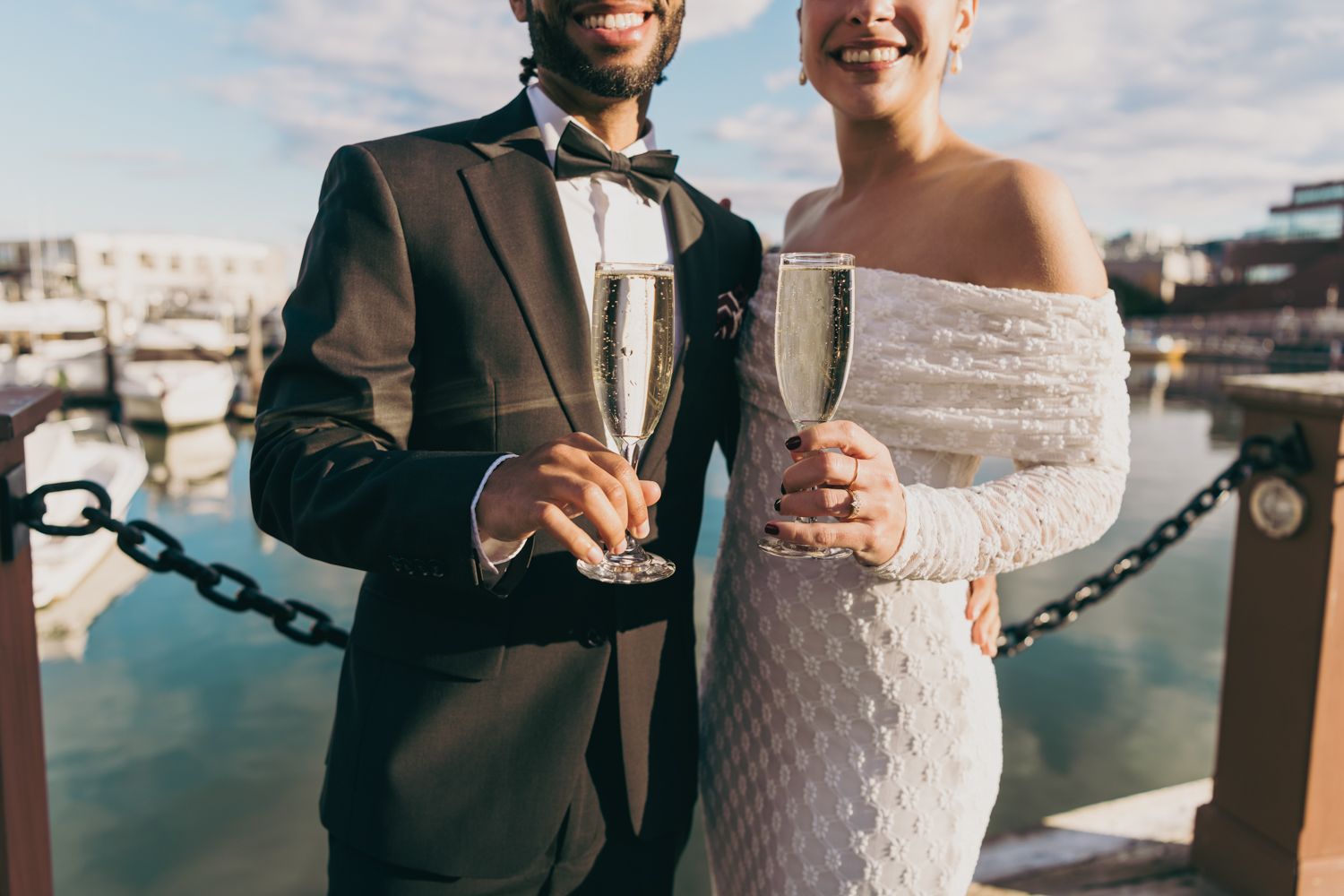 Newlyweds toasting with champagne glasses at a marina on their wedding day.