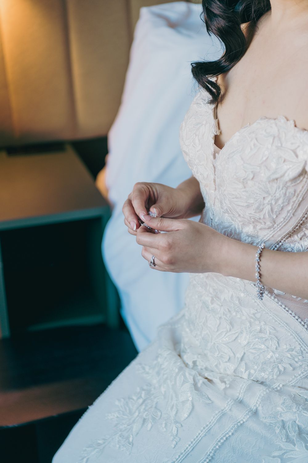 Bride in white lace wedding gown adjusting jewelry, wearing pearl bracelet and necklace.