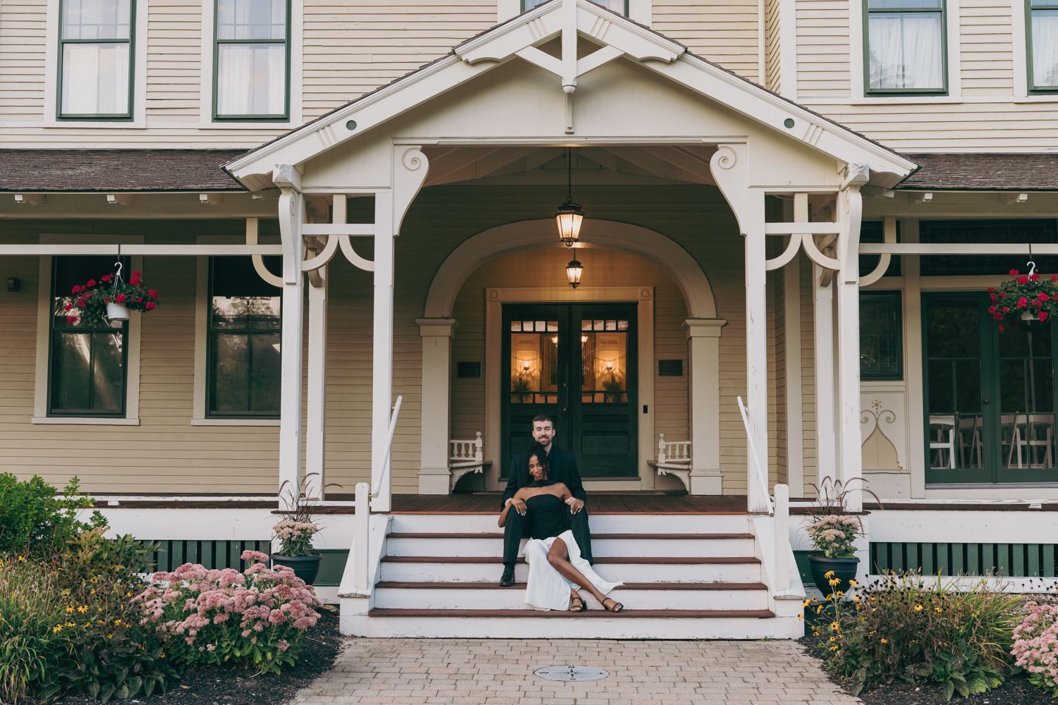Couple sitting on the steps of a charming Victorian home with a covered porch.