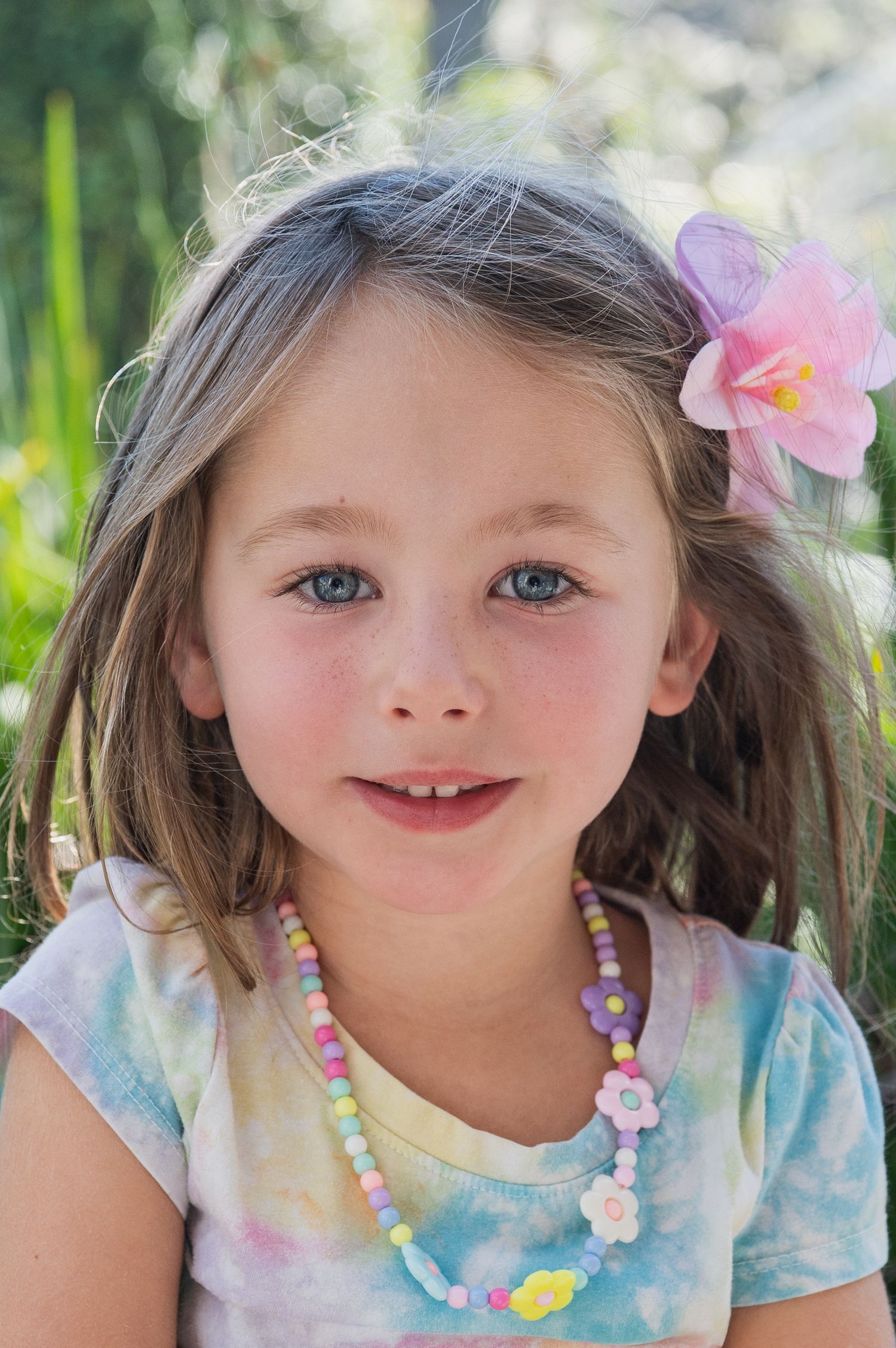 Young girl with flower in hair wearing colorful beaded necklace outdoors.