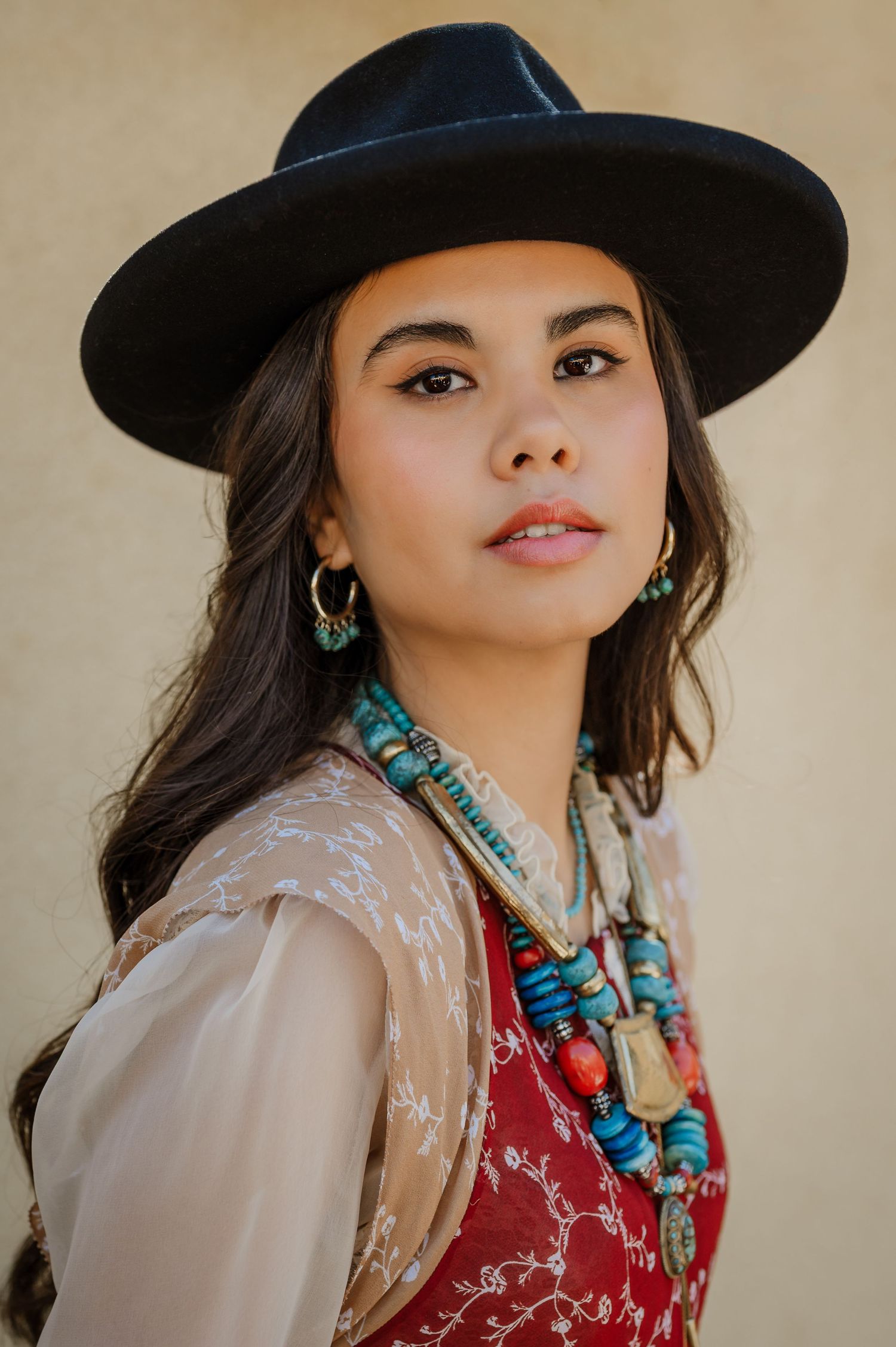 Young woman in black wide-brim hat, turquoise beaded necklace and earrings, red vest, bohemian style portrait.