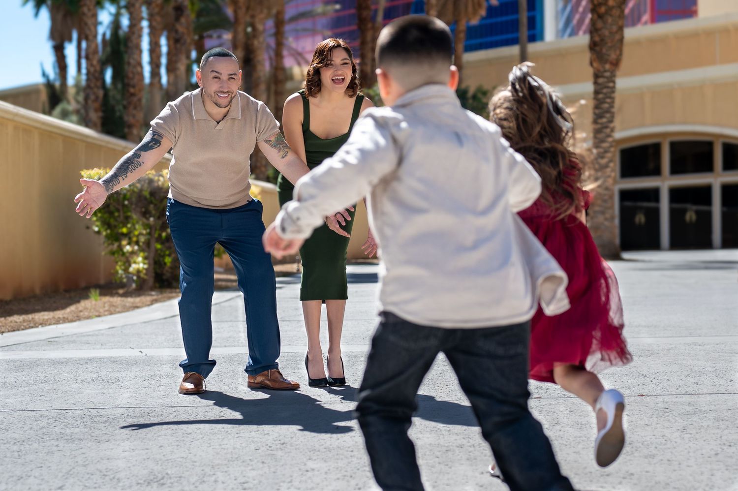 Family reunion outdoors as parents open arms to welcome two children running toward them in a sunny plaza.