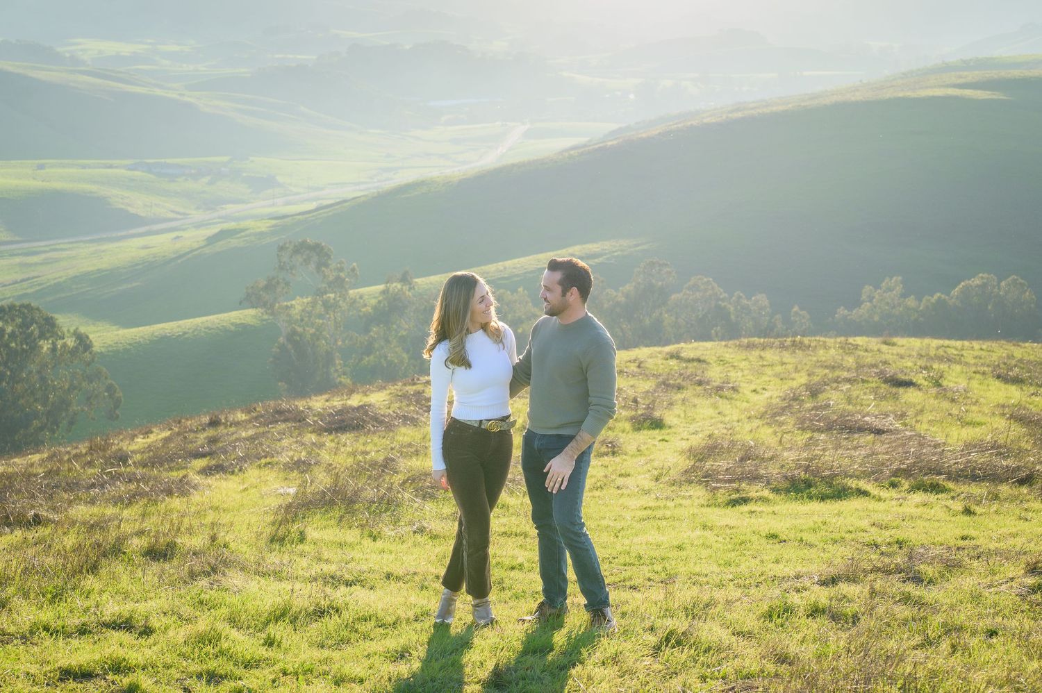Couple standing together on green hillside with scenic valley views.