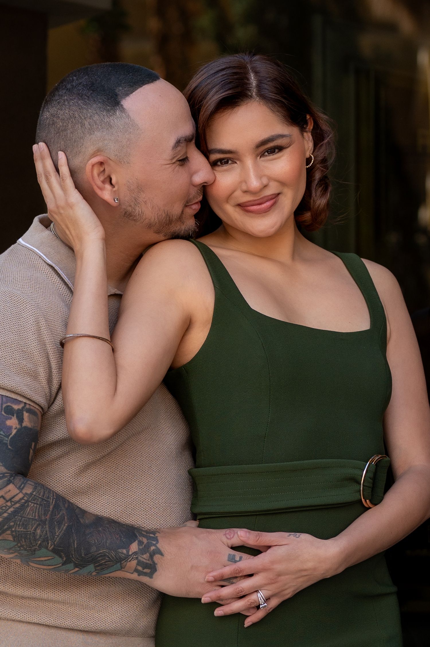 A tattooed man kisses a smiling woman in a green dress during a romantic couples portrait session.
