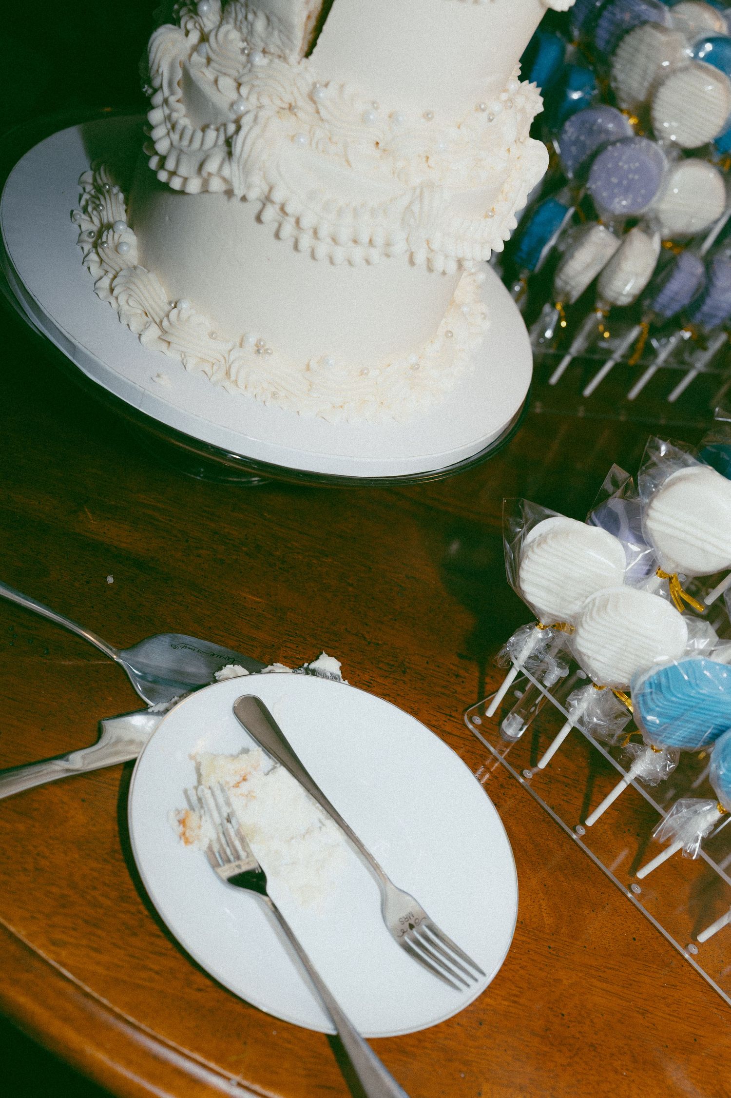 Elegant two-tier white wedding cake with floral details beside blue cake pops on a wooden table.