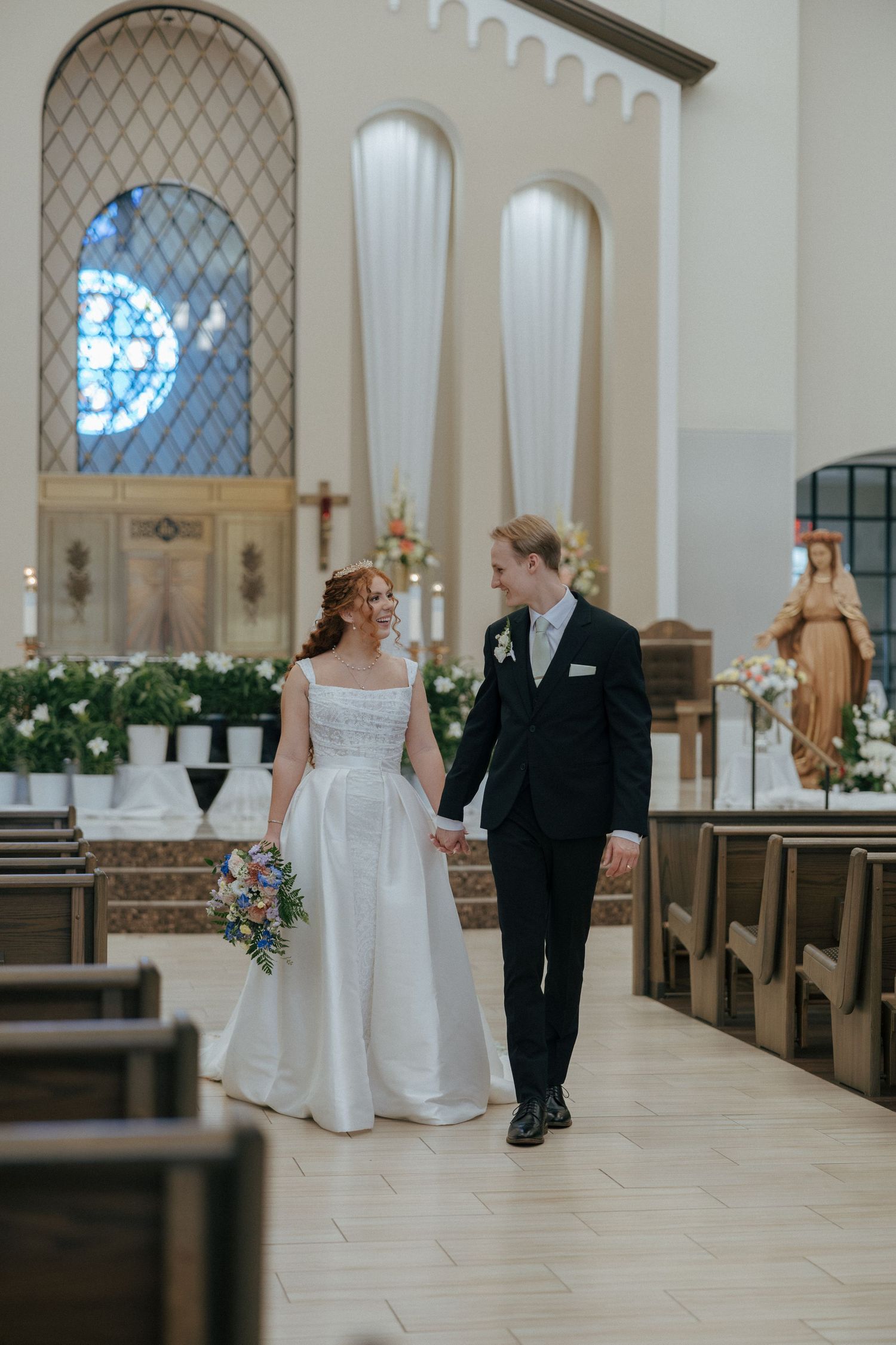 Bride and groom walking hand in hand down the aisle of a beautiful Catholic church.