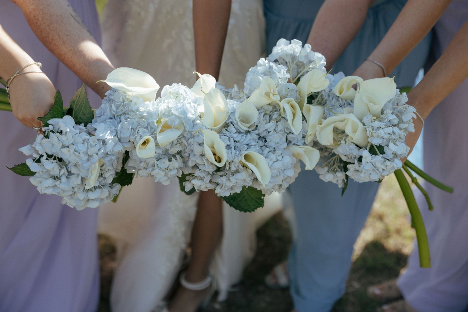 Bridesmaids holding elegant bouquets of white calla lilies and blue hydrangeas at a wedding.
