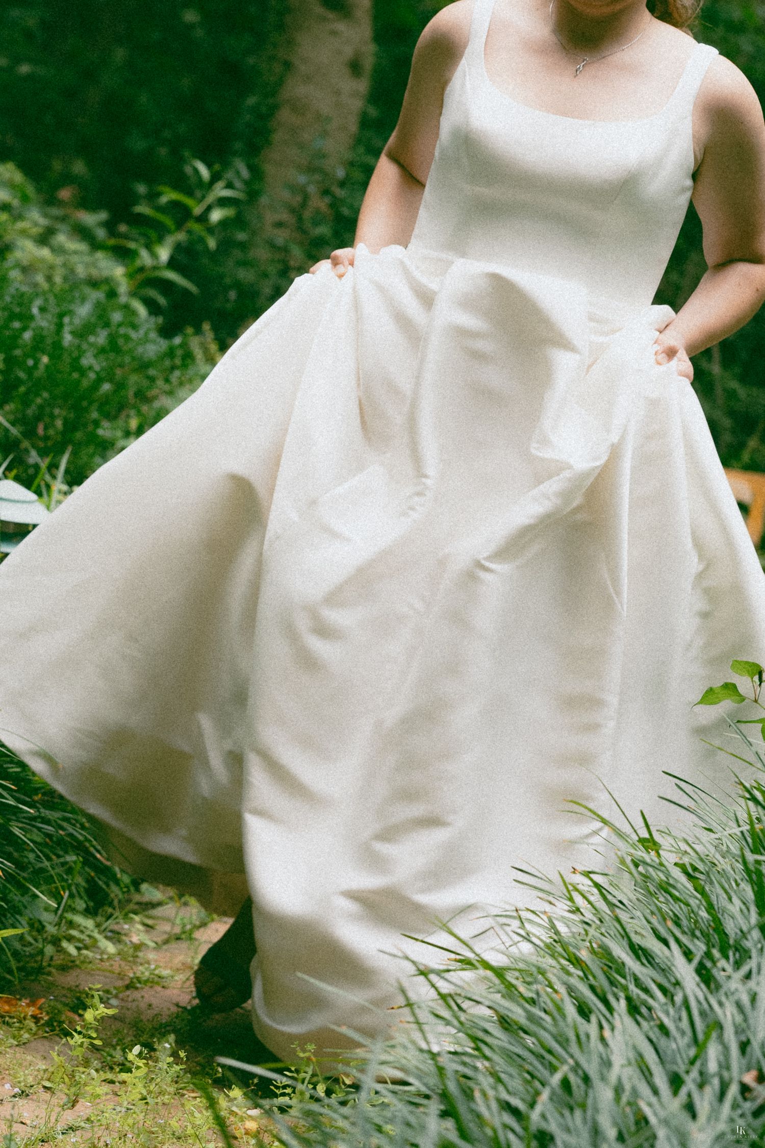 Bride in elegant ivory ball gown wedding dress twirling in lush green garden setting.