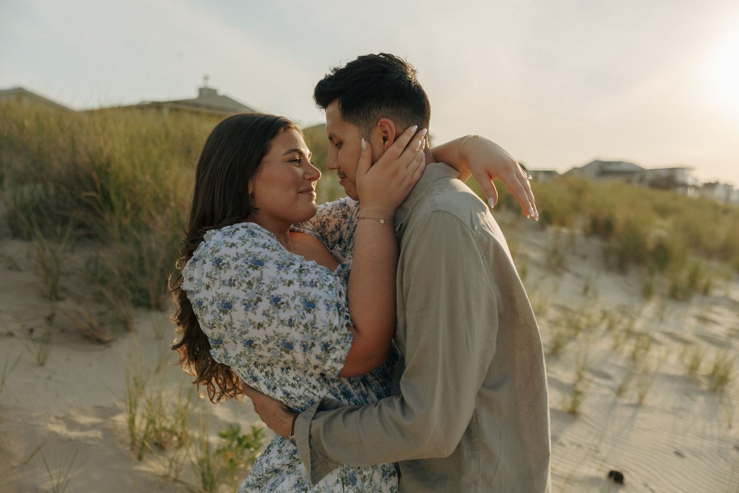 Romantic couple embracing and almost kissing among beach sand dunes during golden hour sunset.