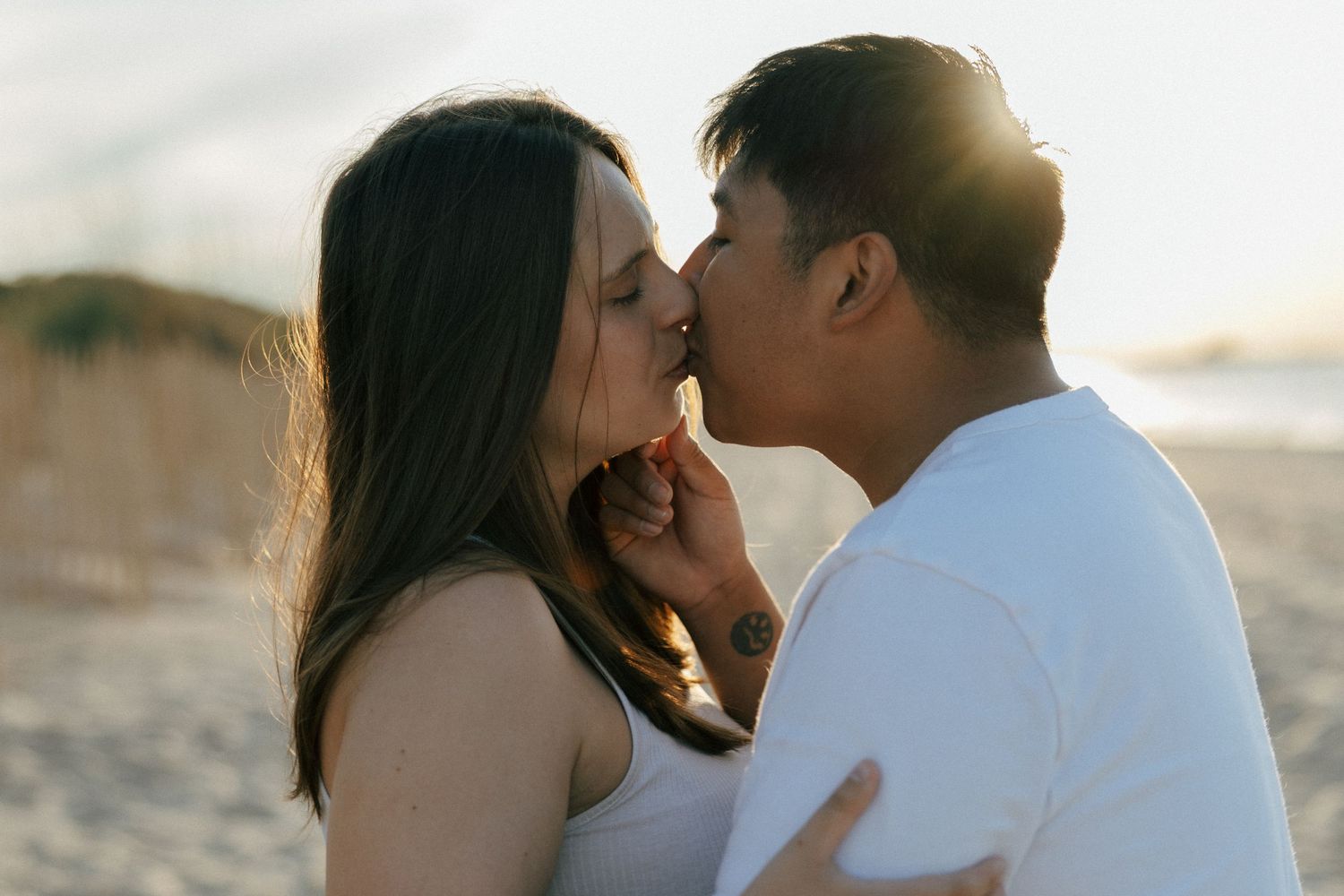 Couple sharing a romantic sunset kiss on a sandy beach with golden backlight.