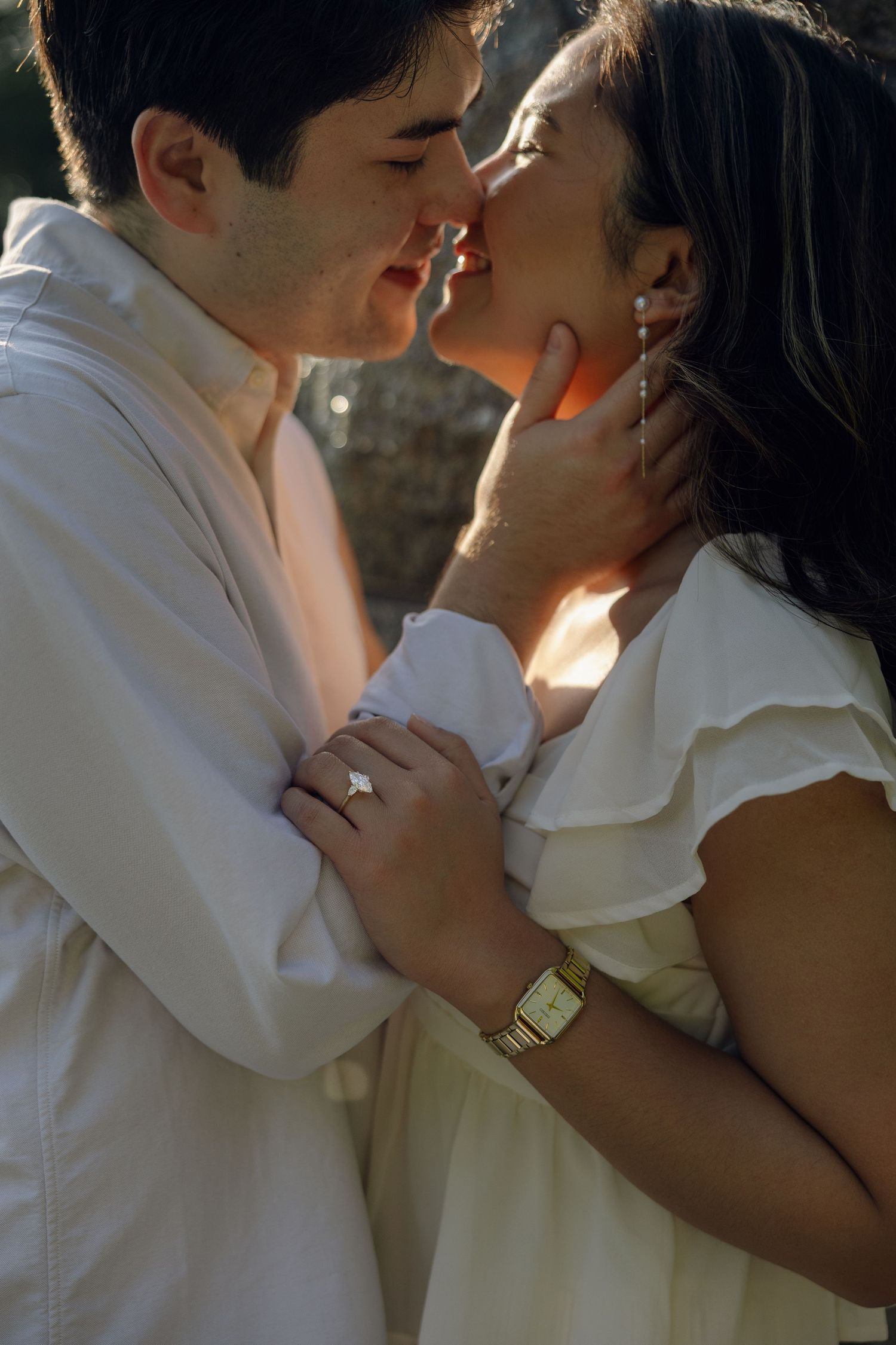 Couple in white outfits sharing a romantic moment, woman wearing diamond ring and gold watch, golden hour lighting.