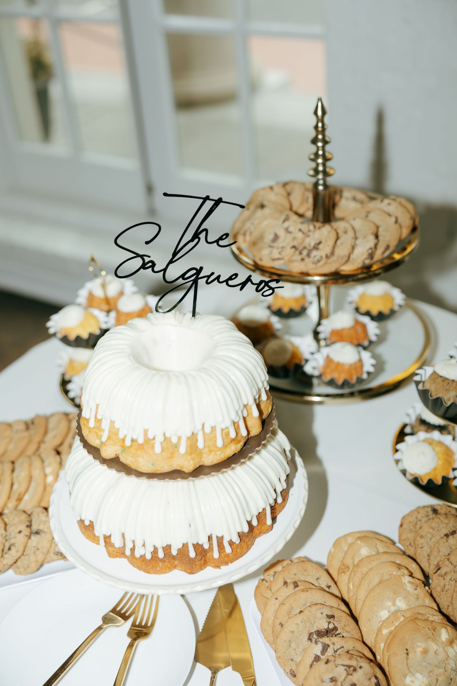 Elegant wedding dessert table with tiered bundt cake, cookies, and The Salgueros cake topper in gold and white.