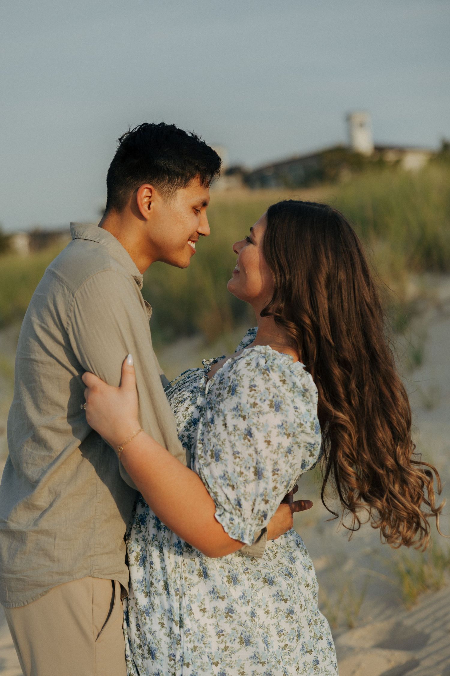 A couple embraces on a sandy beach at golden hour, gazing into each other's eyes romantically.
