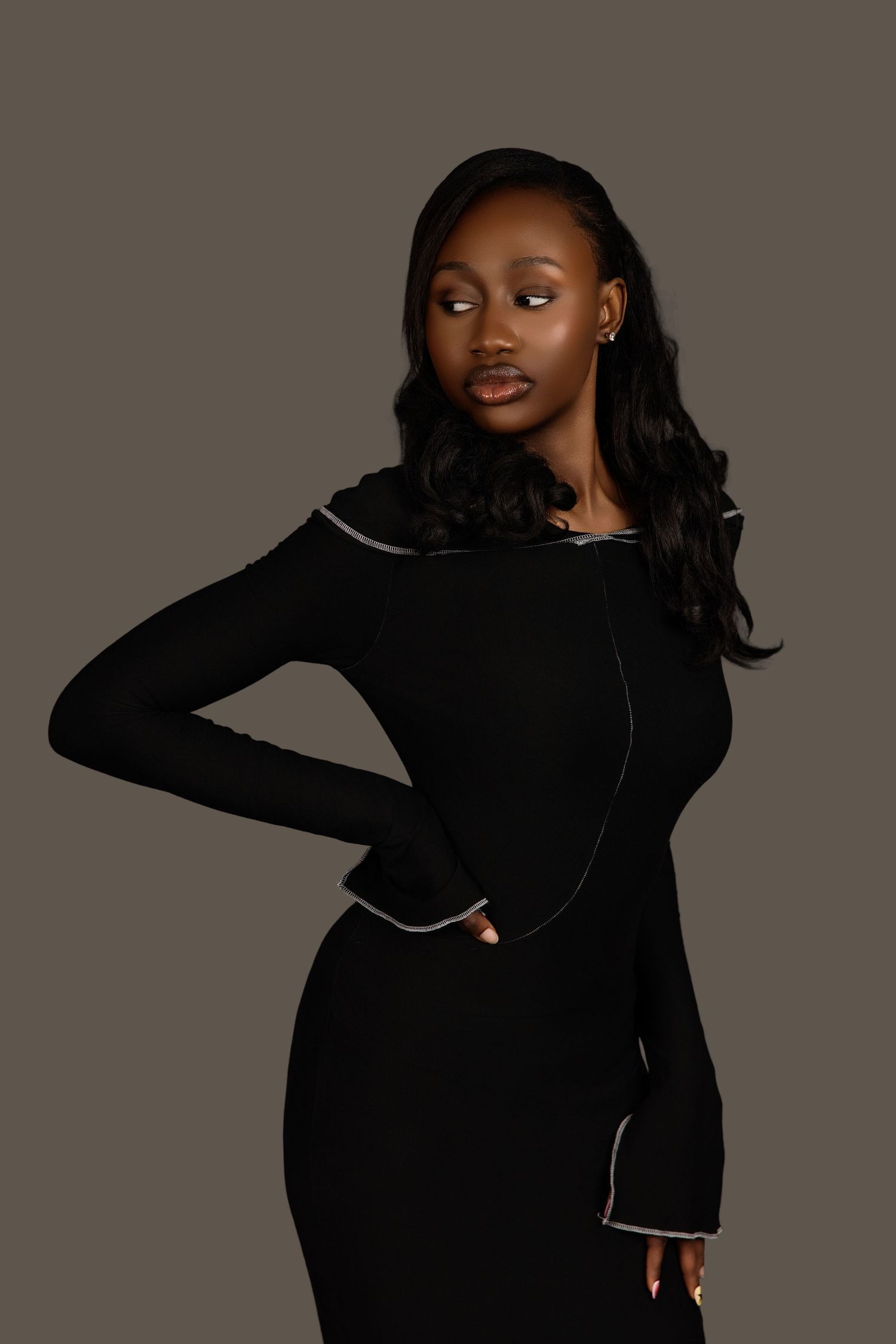 Black female model in black long-sleeve fitted dress with white piping detail, studio photo.