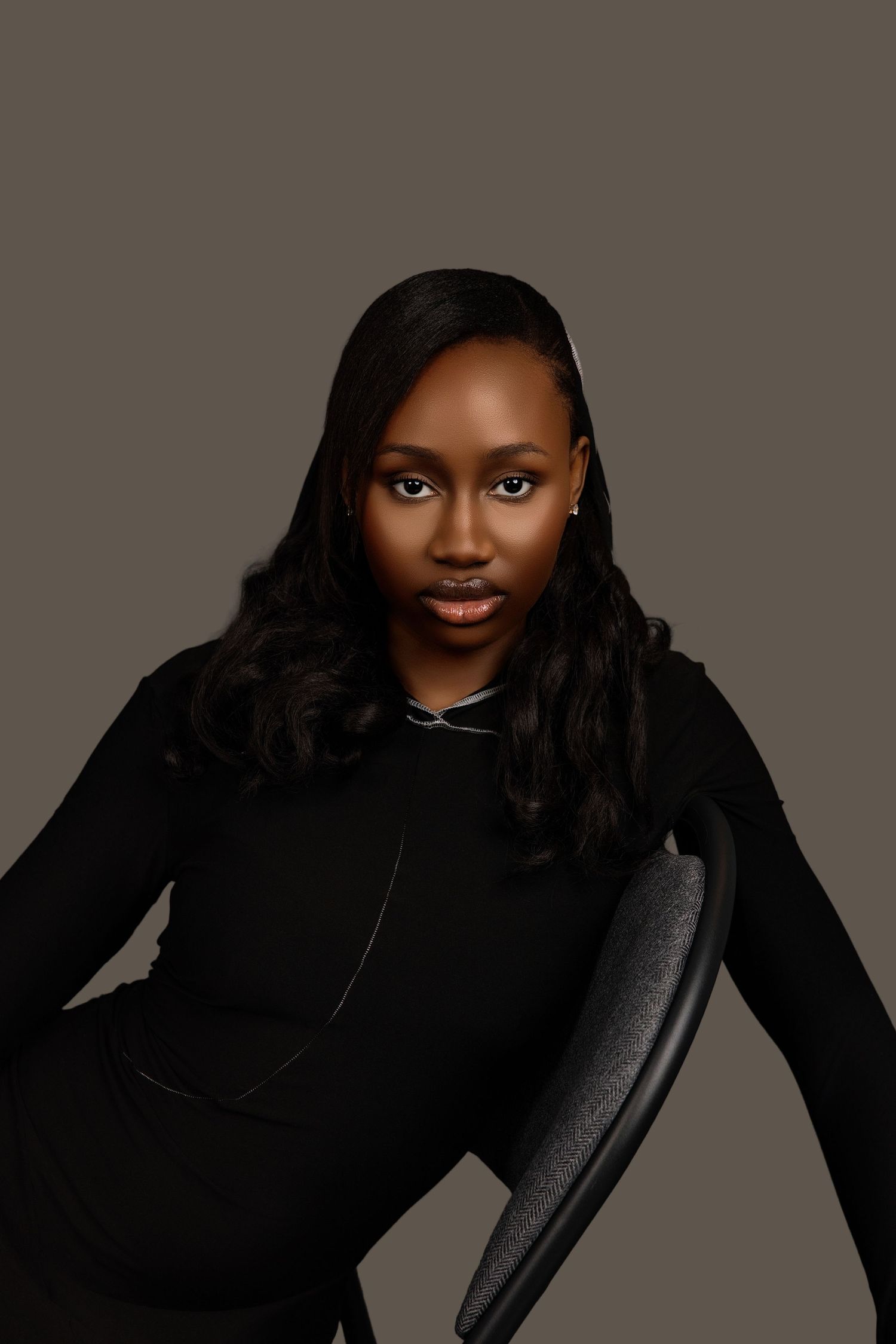 Beautiful Black woman in black long-sleeve dress leaning on chair back, studio portrait.