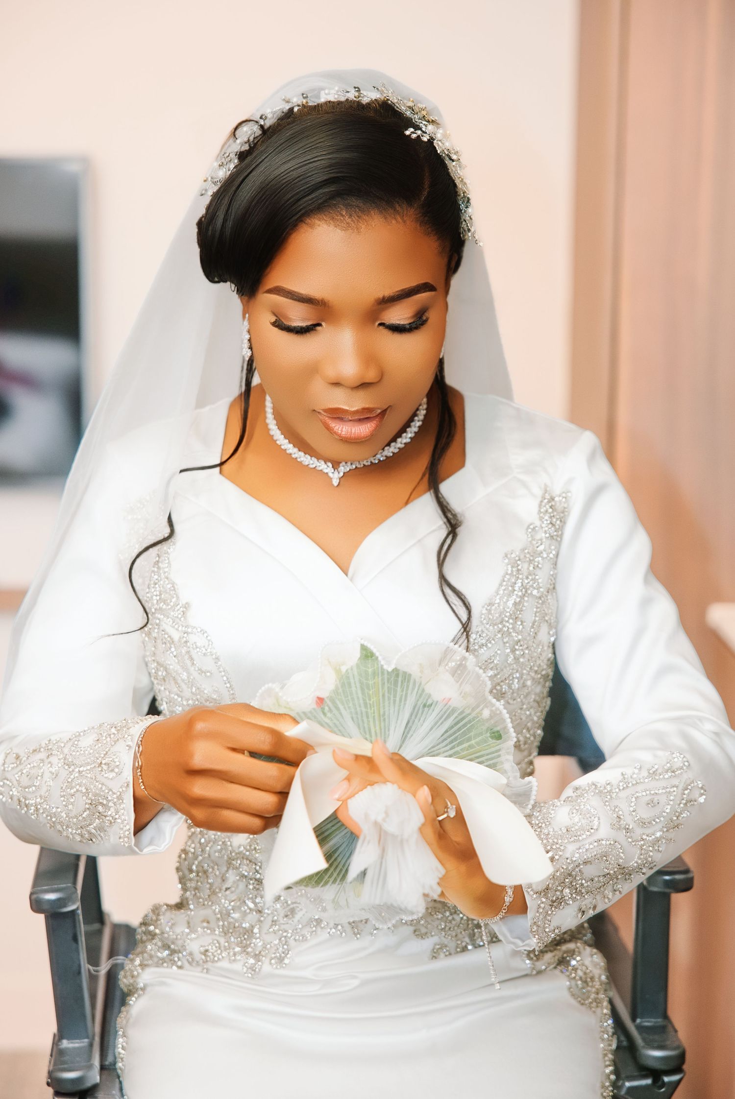 Elegant Black bride in white beaded gown and veil holding bouquet, wearing diamond jewelry on wedding day.