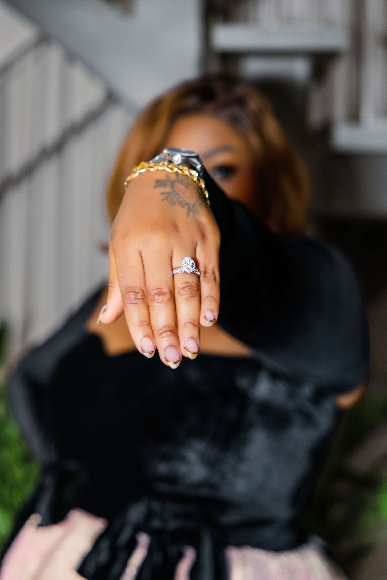Woman showing off a diamond engagement ring on her hand, wearing a black velvet outfit and gold bracelet.