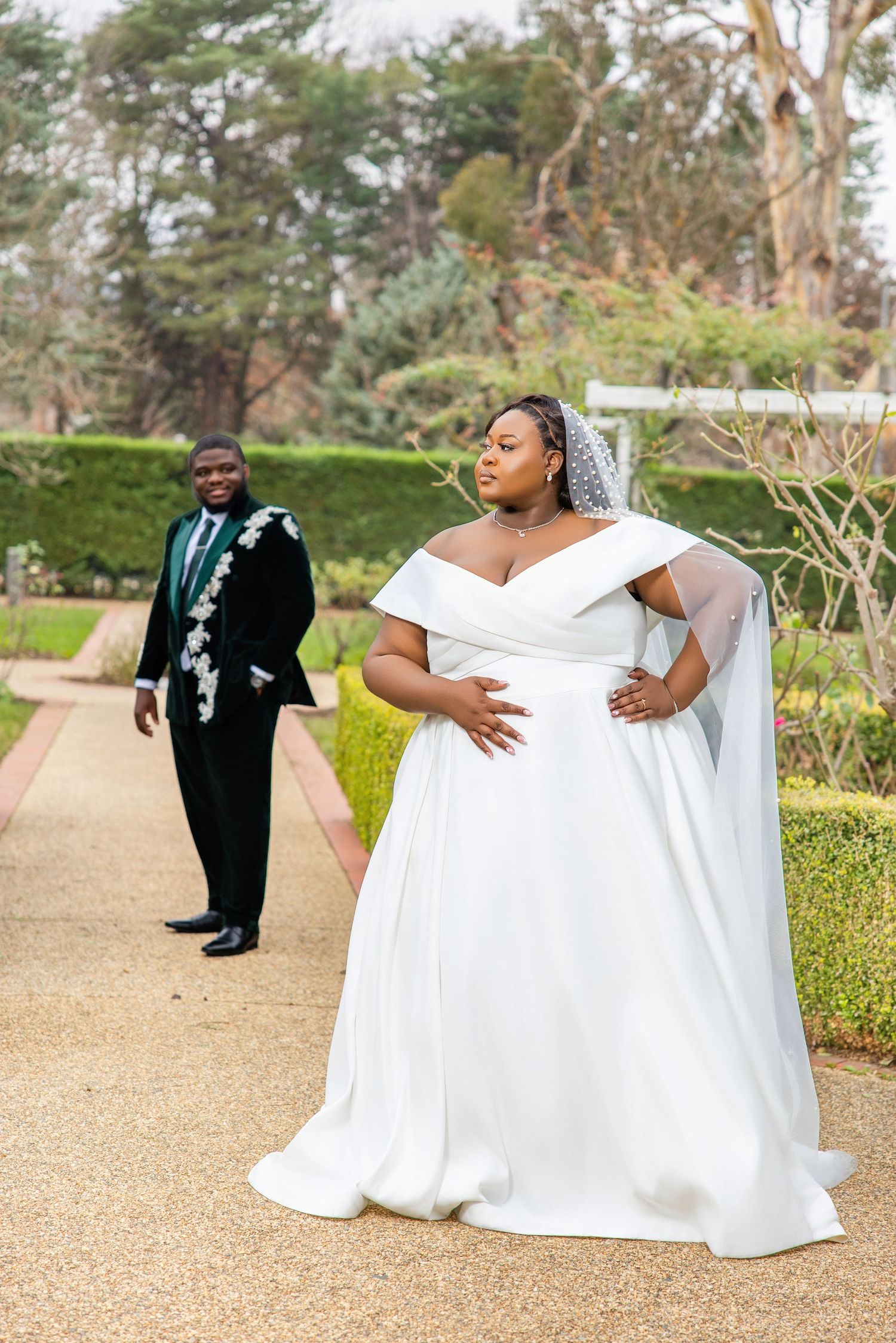 Bride in white ball gown and groom in dark green embroidered tuxedo during outdoor garden wedding photoshoot.