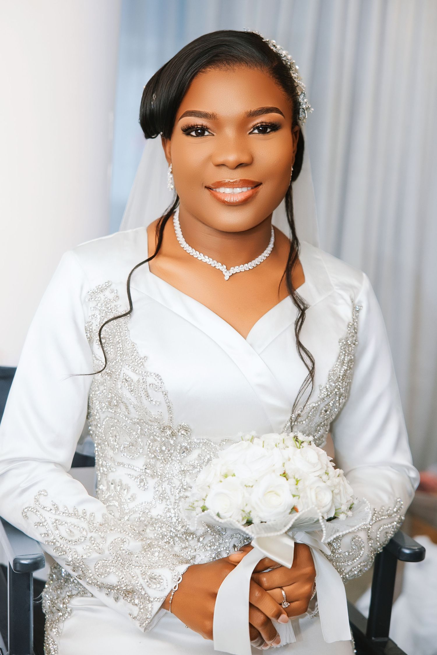 Elegant Black bride in white lace wedding gown holding white bouquet, wearing diamond jewelry and veil.