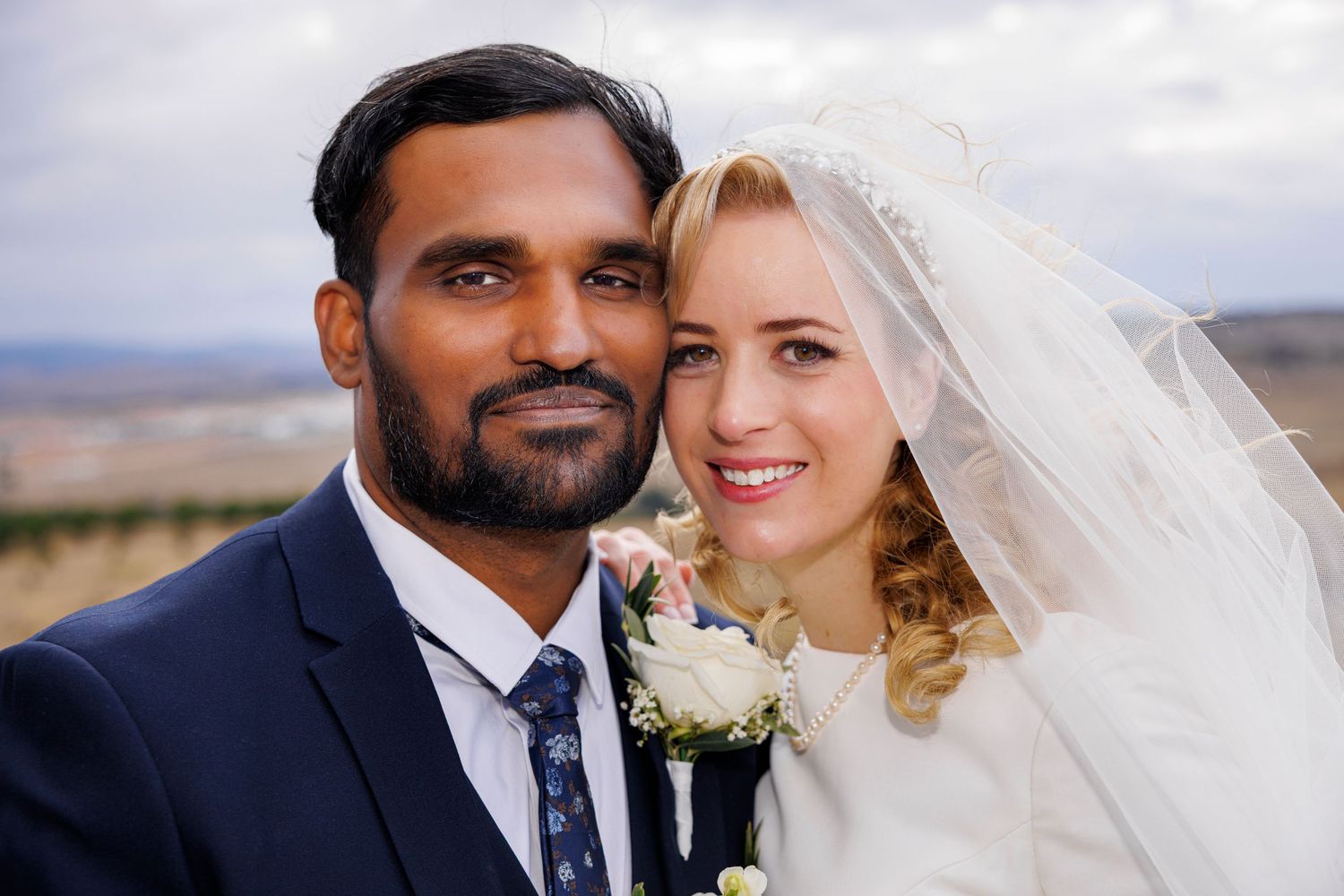 Interracial couple smiling closely together on their wedding day outdoors.