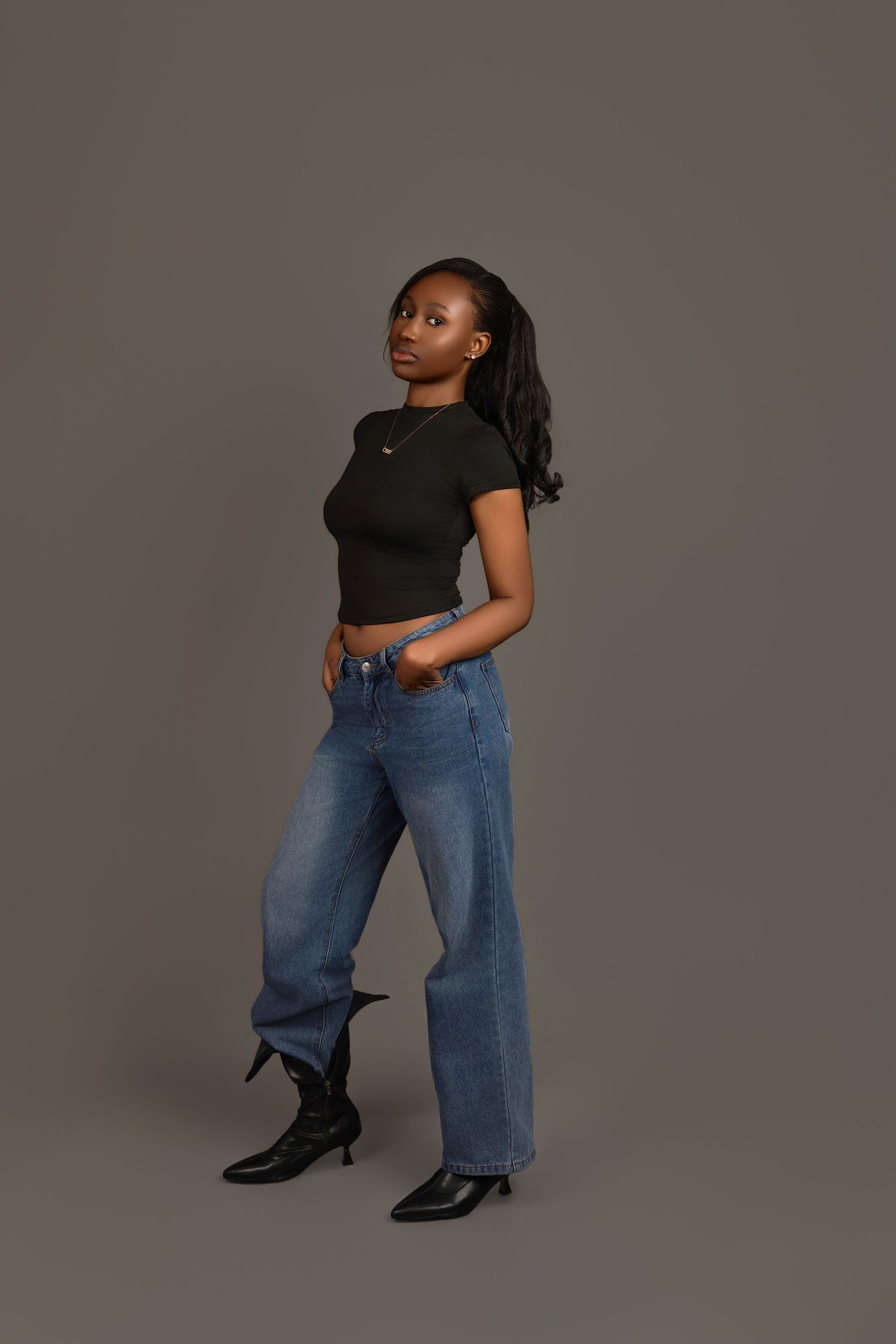 Black woman in black crop top and wide-leg blue jeans with black heeled boots, studio shot.