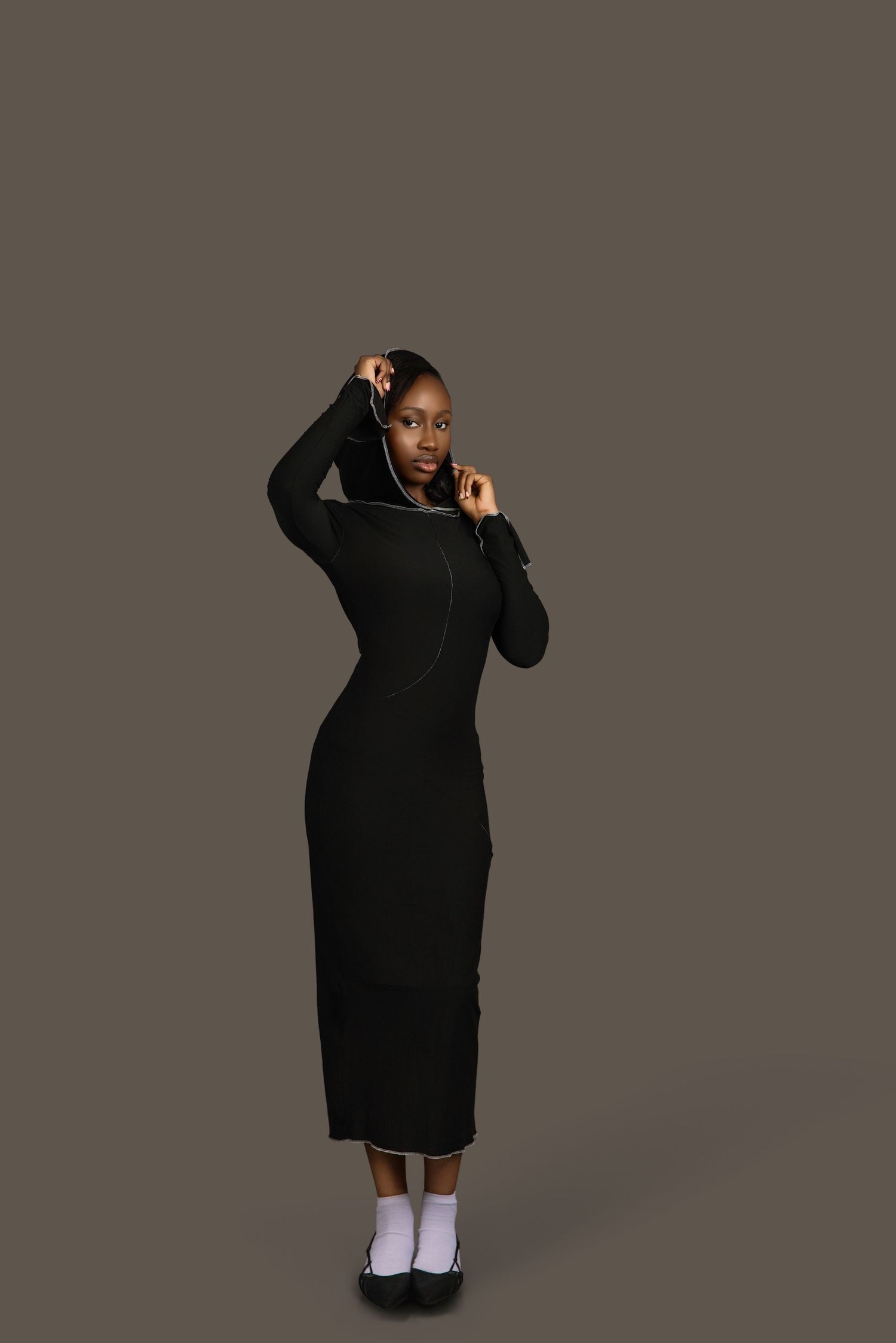 Full-length portrait of Black woman in black hooded midi dress, studio fashion photography.