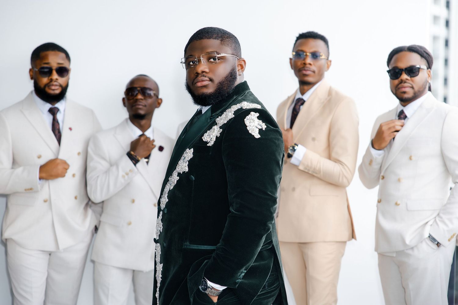 A groom in a green velvet floral suit poses confidently with four groomsmen in beige suits behind him.