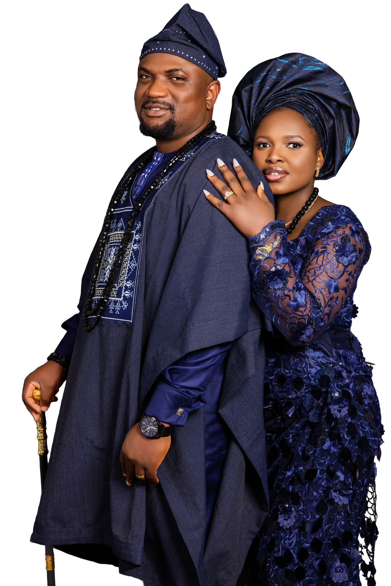 A couple in matching navy blue Nigerian traditional Yoruba attire, the man holding a cane and woman in gele headwrap.
