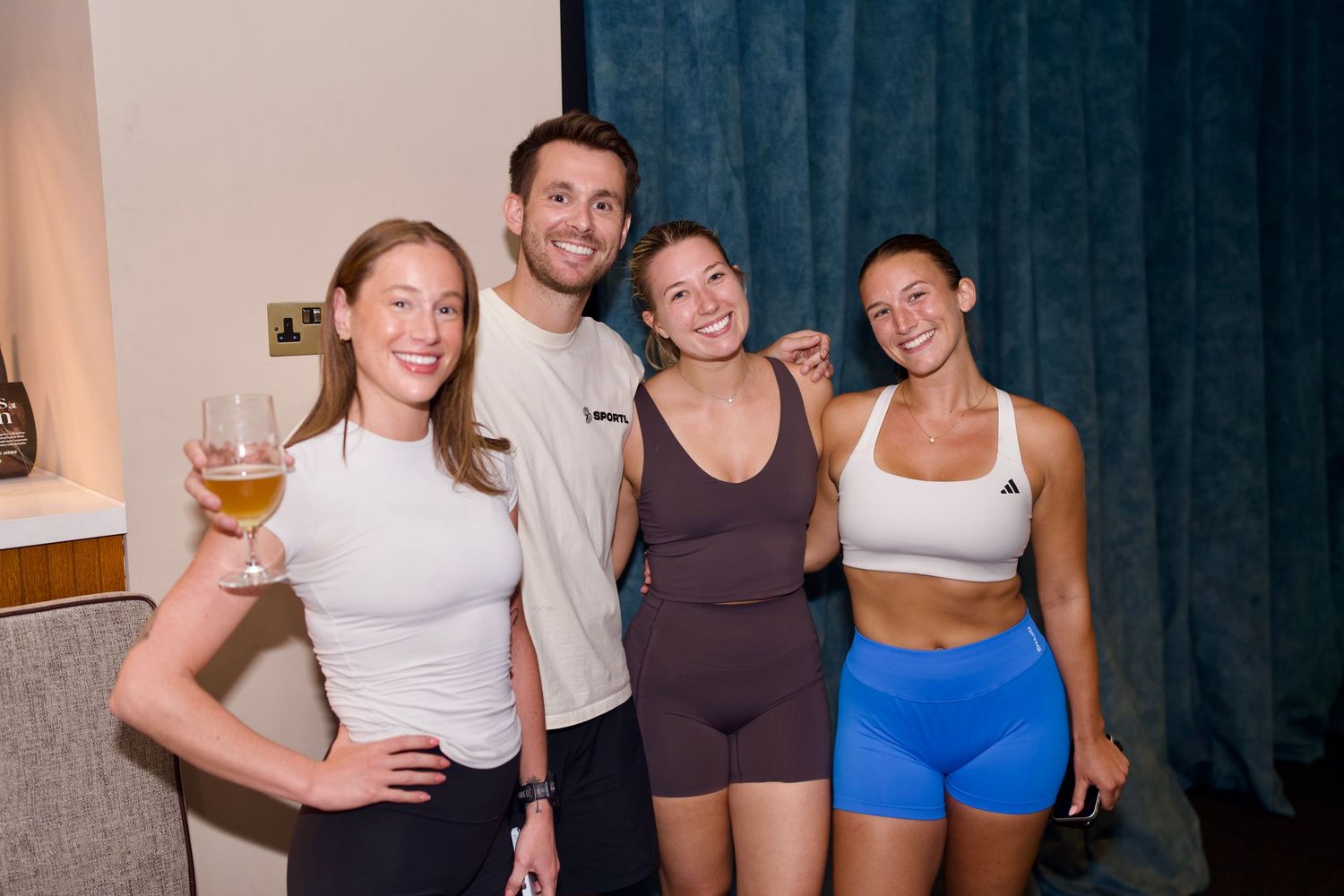 Group of four athletic friends in activewear smiling together at an indoor venue by ARIETA Studios.