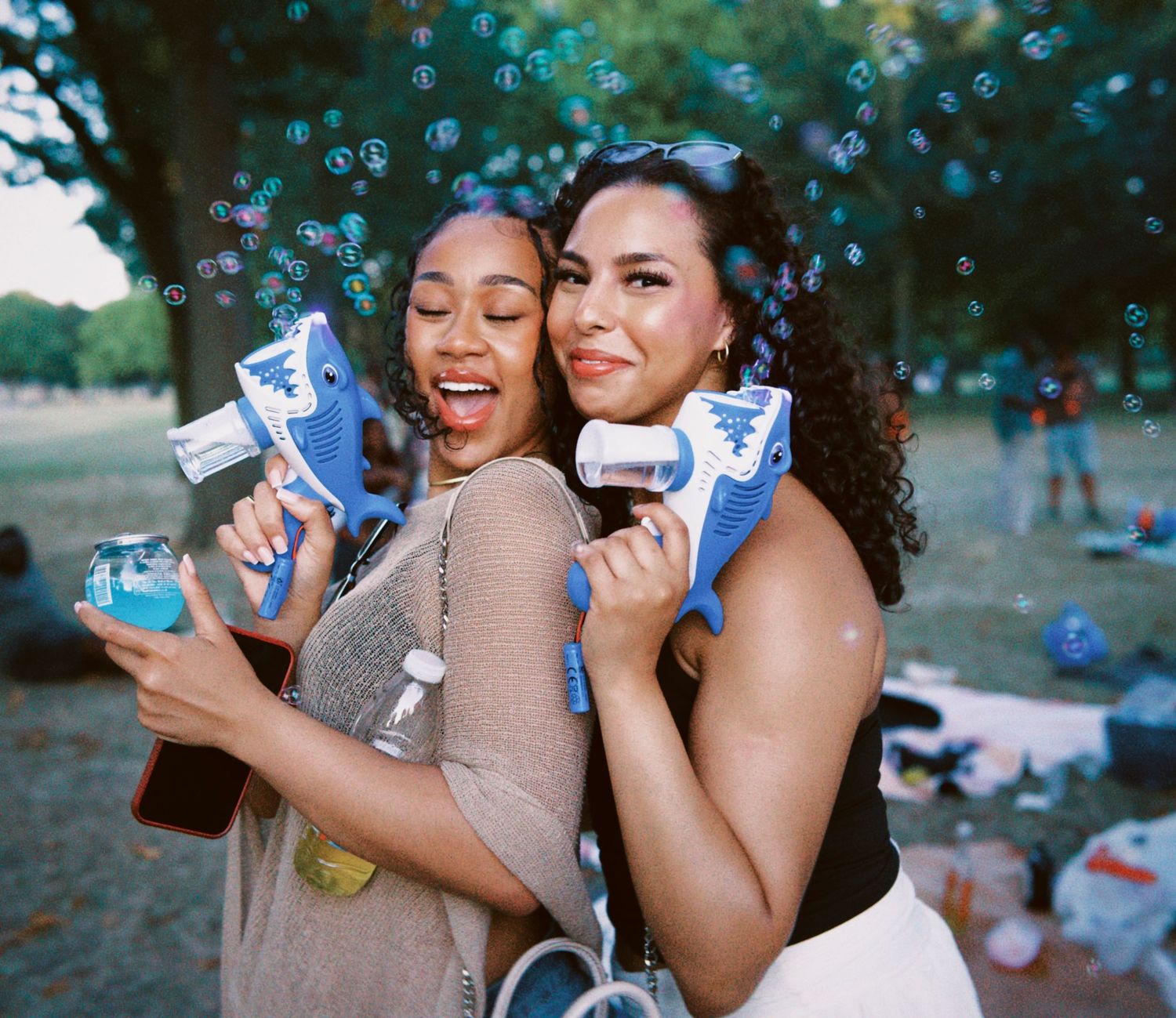 Two women holding blue water guns posing at outdoor London summer event by ARIETA Studios.