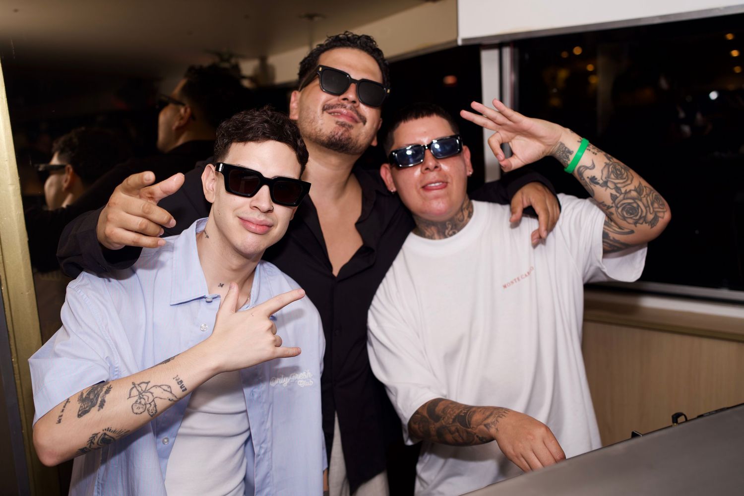 Luigi Sanchez, DJ Khriz, and a friend flashing hand signs and smiling behind the DJ booth setup.