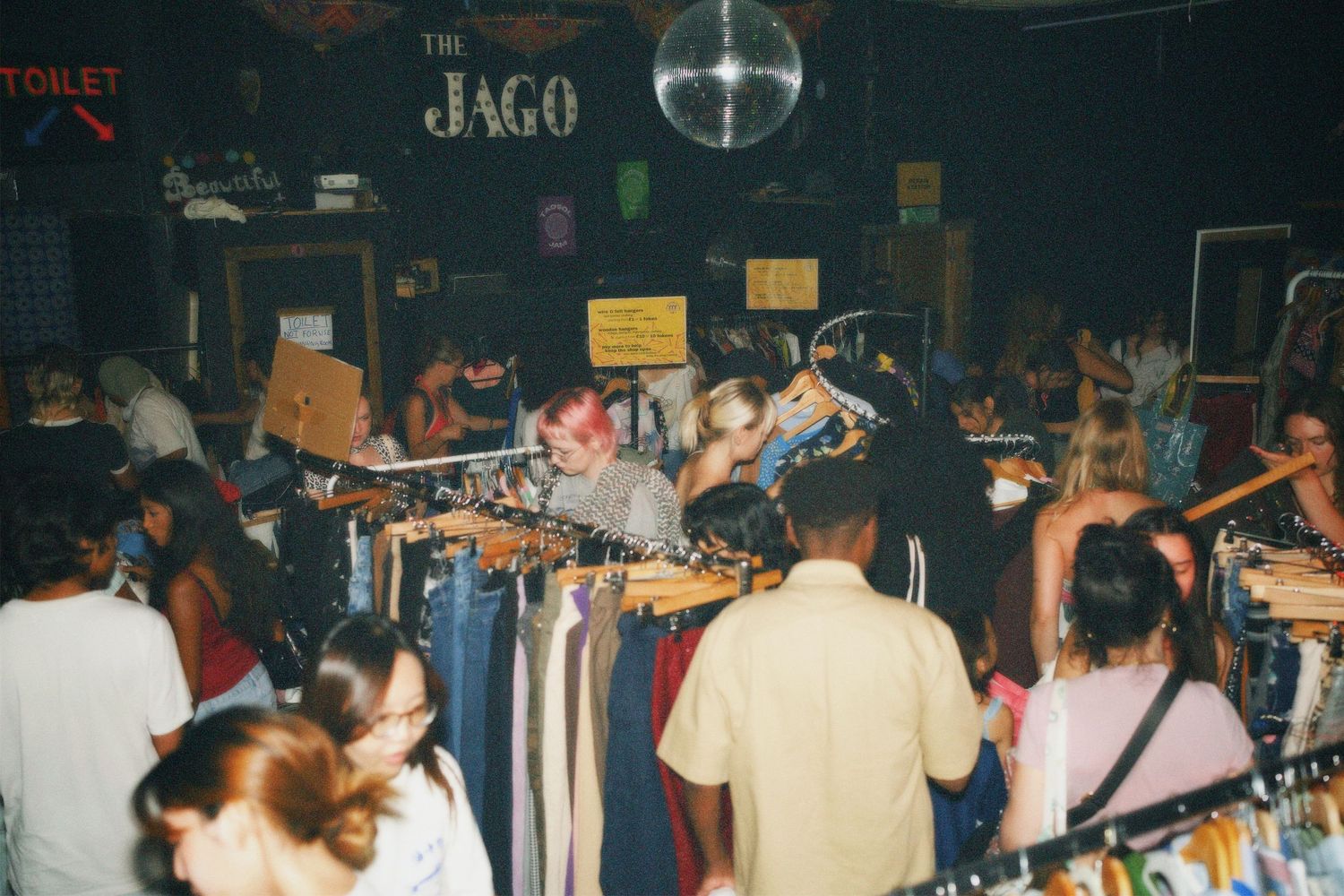Event-goers browsing vintage and pre-loved garments near the DJ booth and disco ball at Fashion For Future swap