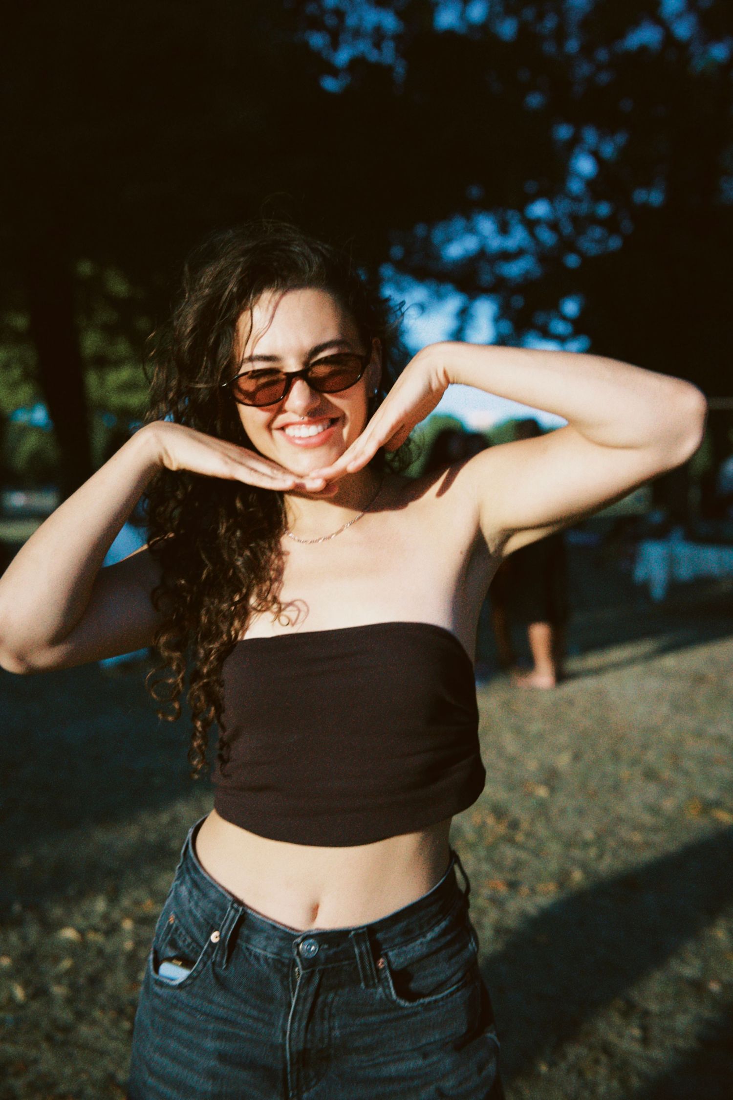 Woman posing playfully in sunglasses at outdoor summer party in London captured by ARIETA Studios.