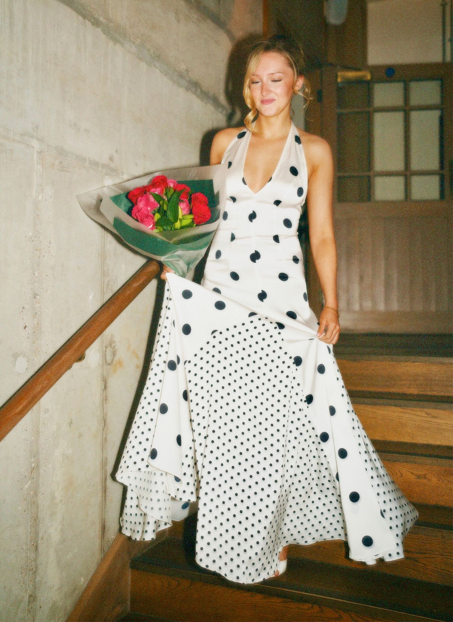 Amelia the celebrant in polka dot dress holding flowers on stairs at Amelia Hurst 21st birthday event by ARIETA Studios.