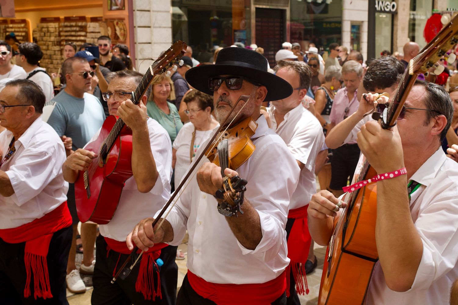 Musicians playing Spanish guitars and violin surrounded by a lively daytime crowd during the street festival in Málaga.