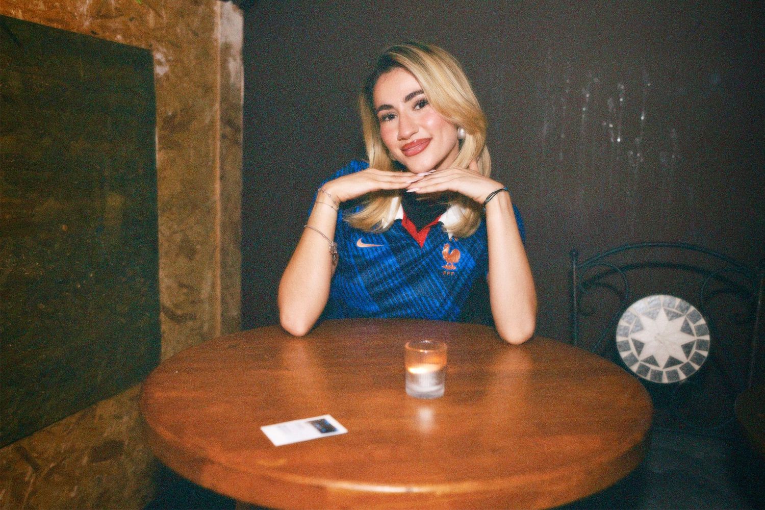 Woman in blue football shirt posing at table at Soho event by ARIETA Studios.