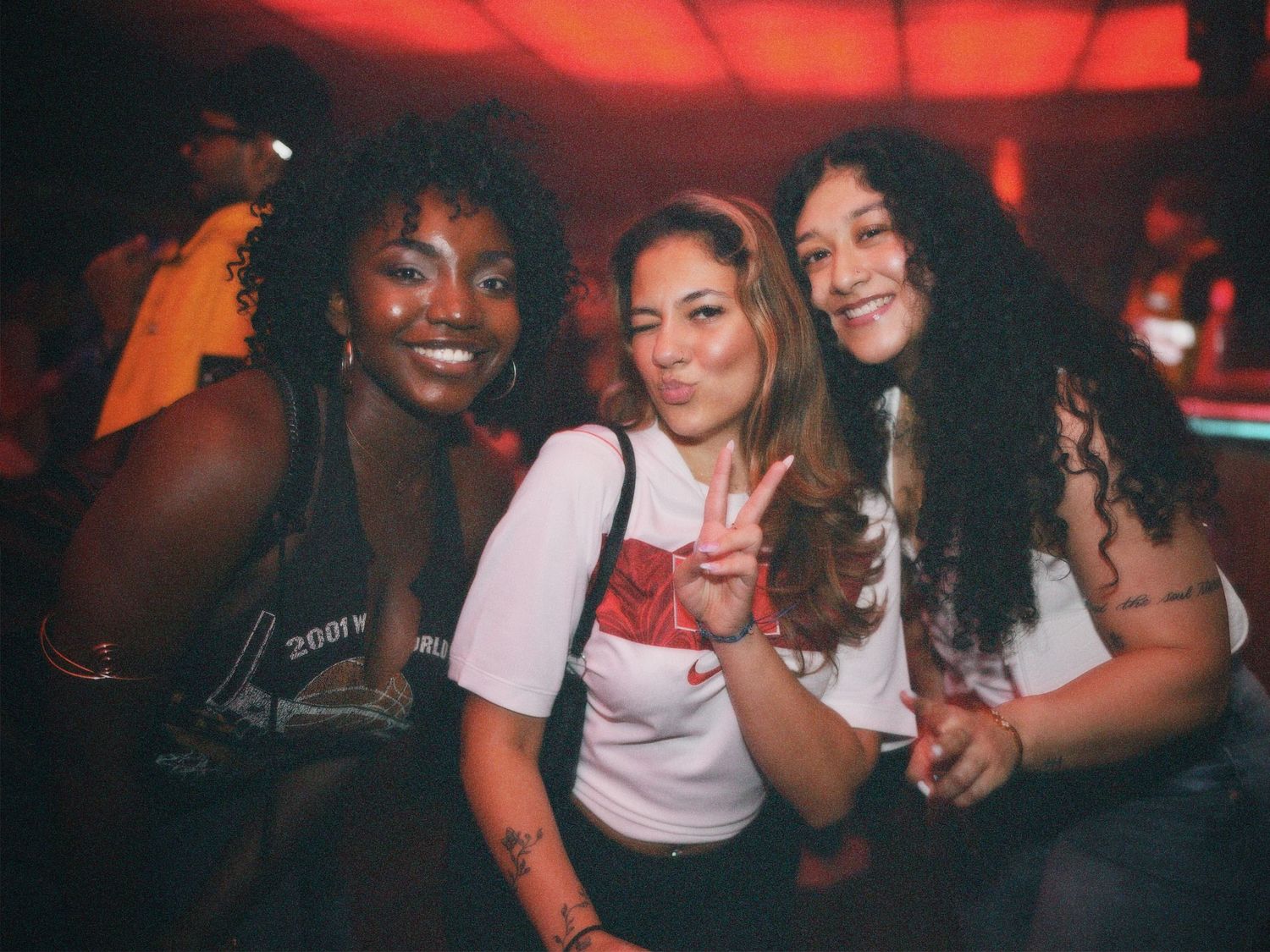 Three friends posing together under red atmospheric club lights by ARIETA Studios.