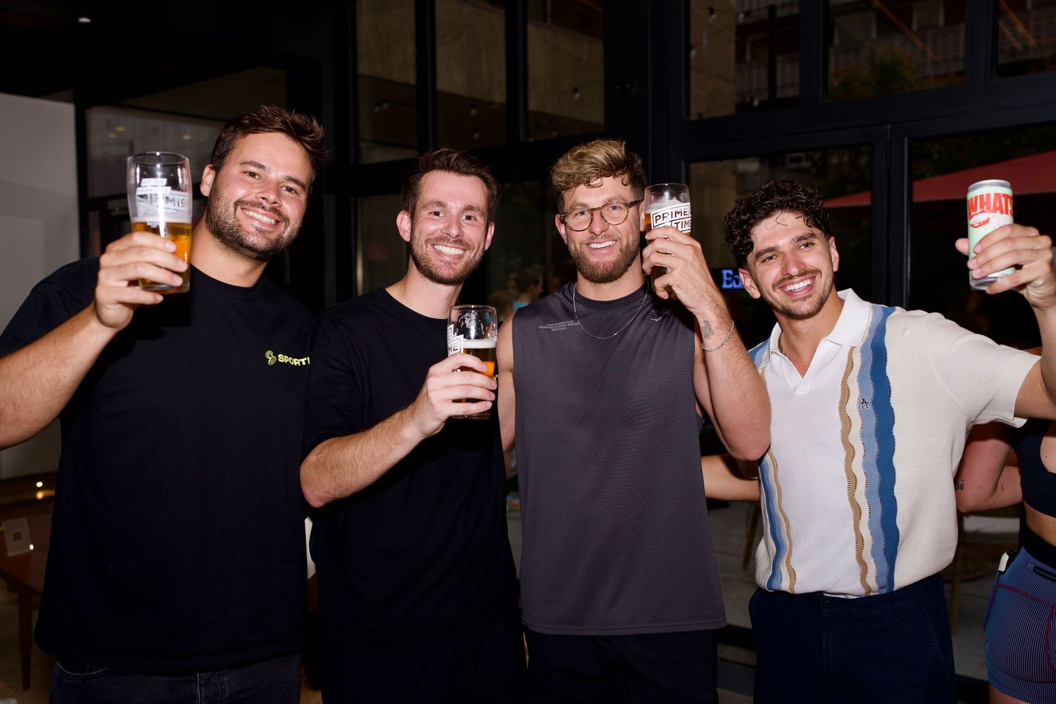 Four men holding drinks and cheering together at London party event by ARIETA Studios.
