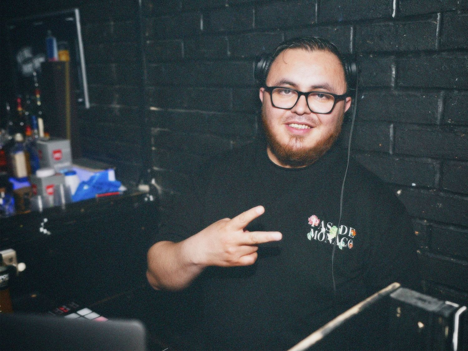 DJ wearing glasses giving peace sign in booth at Paradise Super Club by ARIETA Studios.