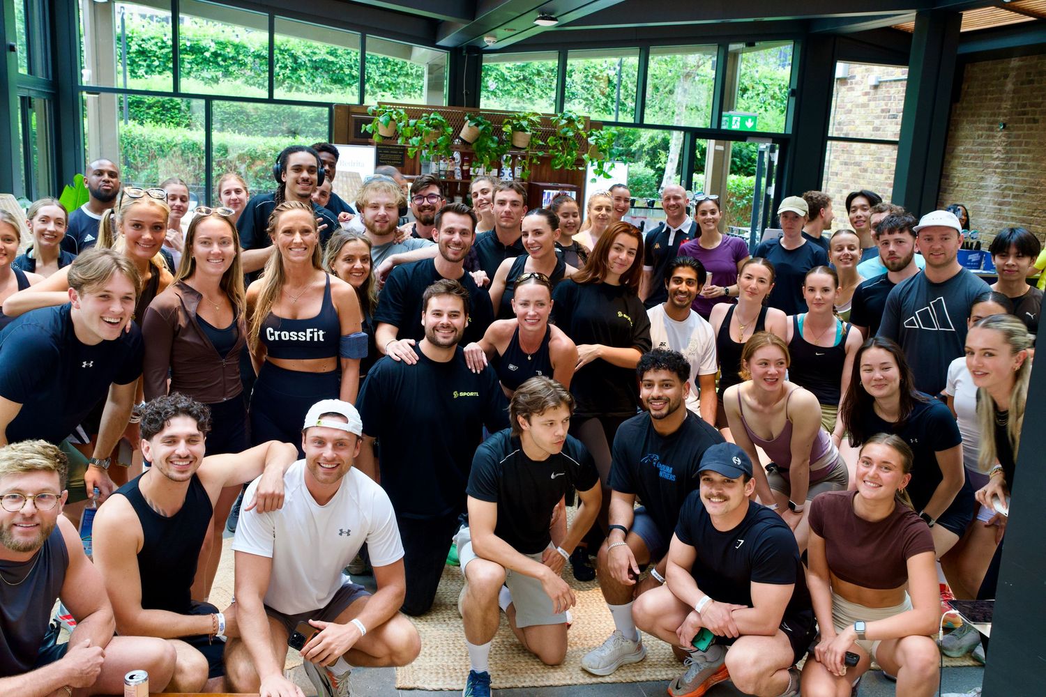Large group of fitness community members smiling together inside a bright London venue. High-end lifestyle photo by ARIETA Studios.