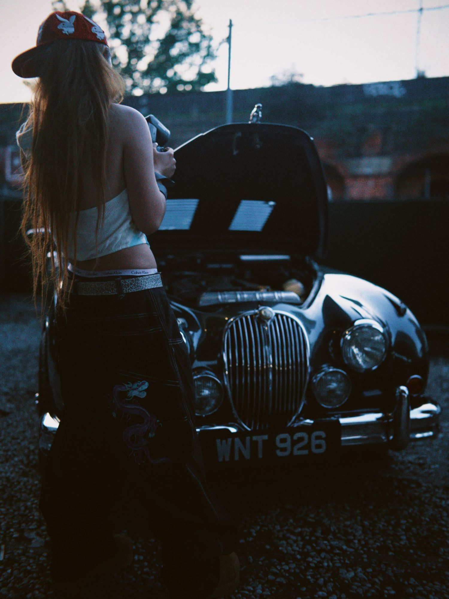 A person standing by an open bonnet of a classic black Jaguar car.