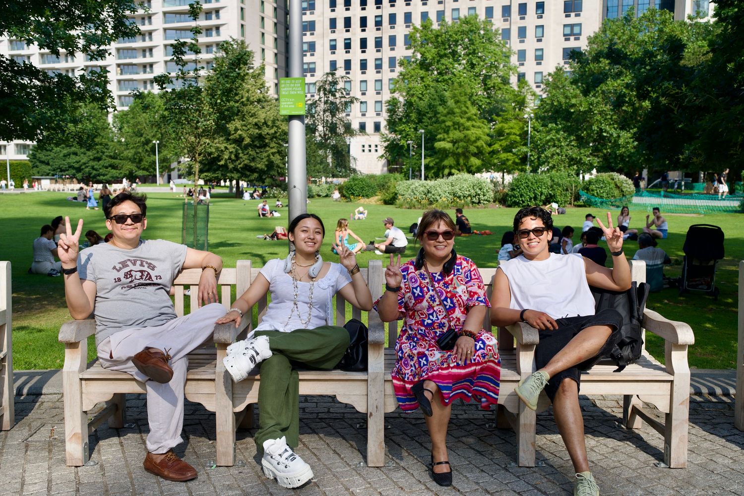 Two candid street photos of a family interacting and flashing peace signs on a wooden park bench in a London square.