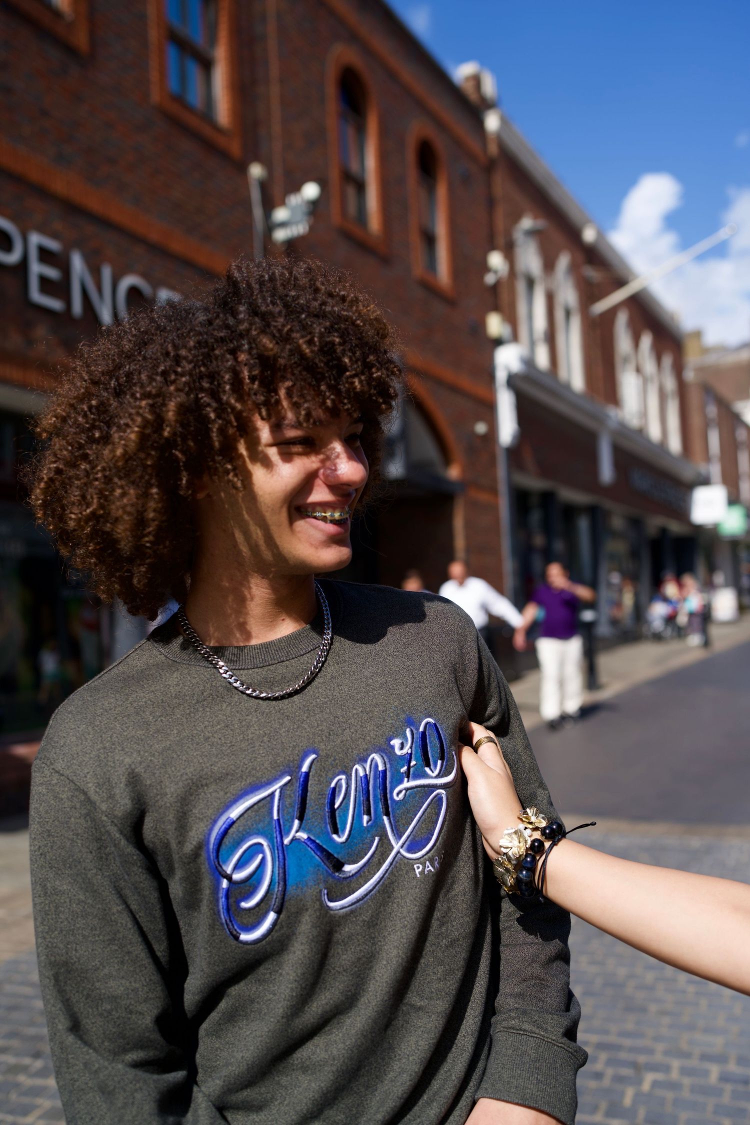 Teen boy in a graphic sweatshirt laughing mid-conversation on the high street.