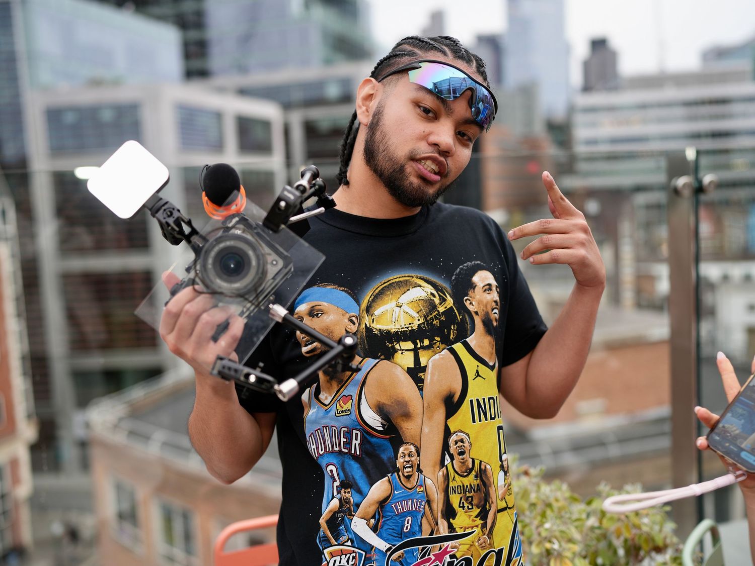 A videographer holding a professional cinema camera rig with a top-mounted light on a city rooftop.