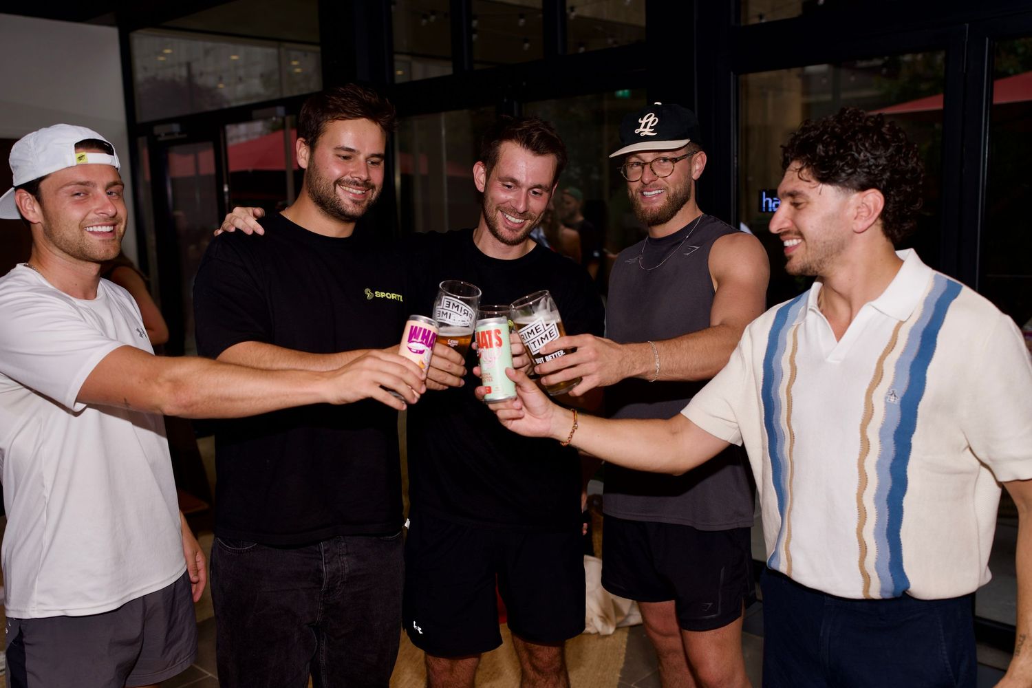 A group of men clinking glasses and WhatsUp Vodka Iced Tea cans in a celebratory toast at a brand after-party. Photo by ARIETA Studios.