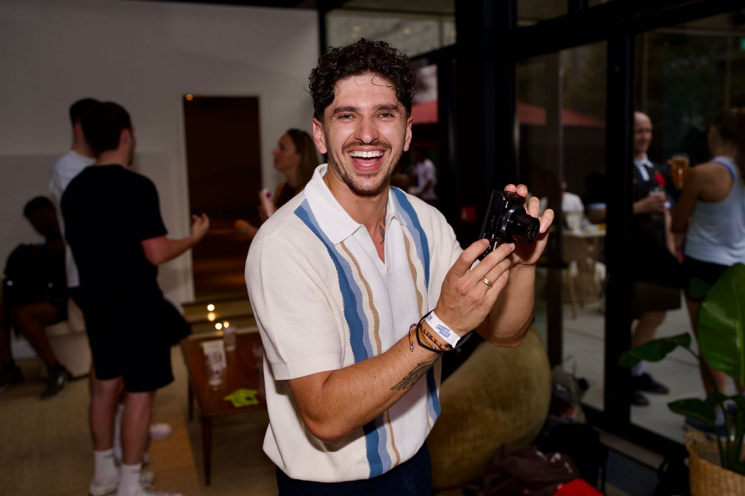 A smiling man in a knit shirt holding a compact camera at a lively commercial brand activation. Photo by ARIETA Studios.