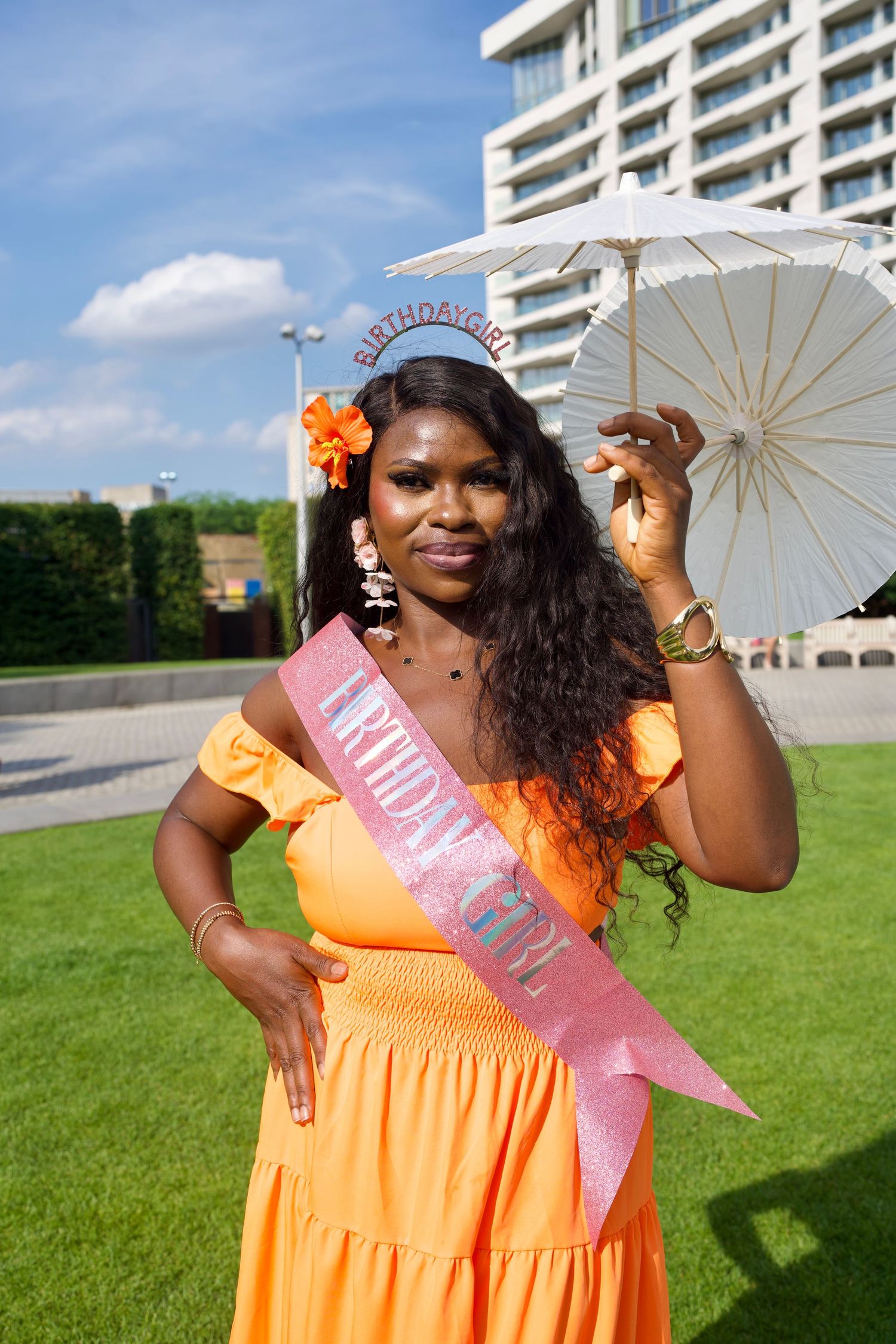 Woman wearing birthday sash holding drink outdoors at garden event by ARIETA Studios.
